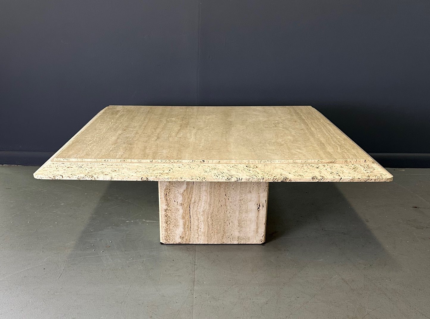 1970s square coffee table crafted from natural travertine stone, featuring a thick slab top with raw, unhoned edges and subtle veining, supported by a sturdy pedestal base for a sculptural, minimalist aesthetic