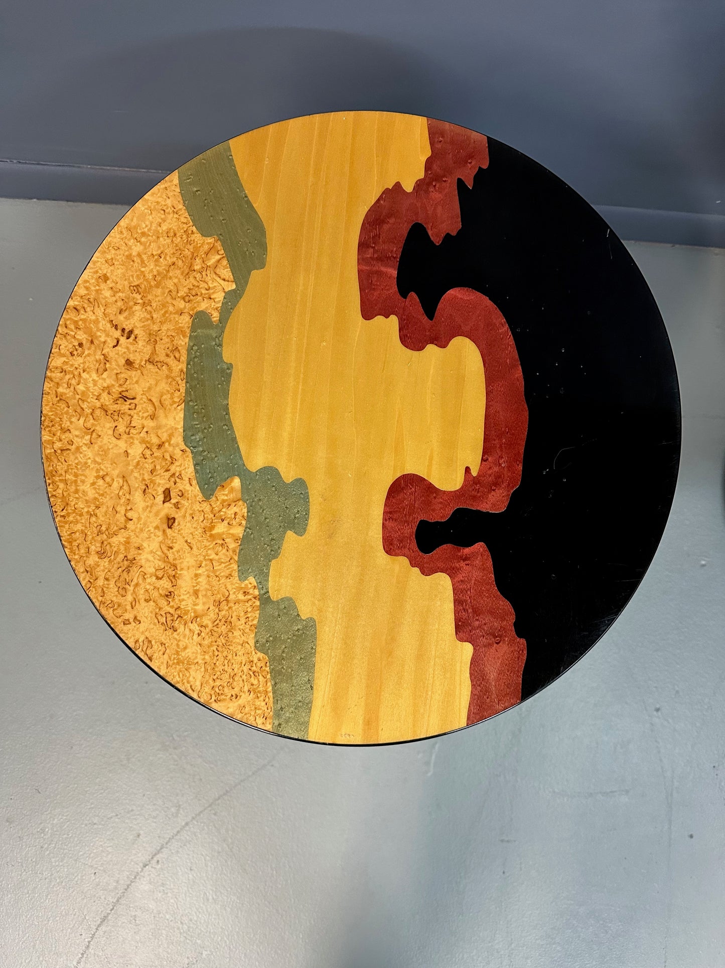 Pair of Carlo Malnati style Postmodern side tables featuring round inlaid wood tops with abstract, multicolored organic patterns and sleek black pedestal bases.