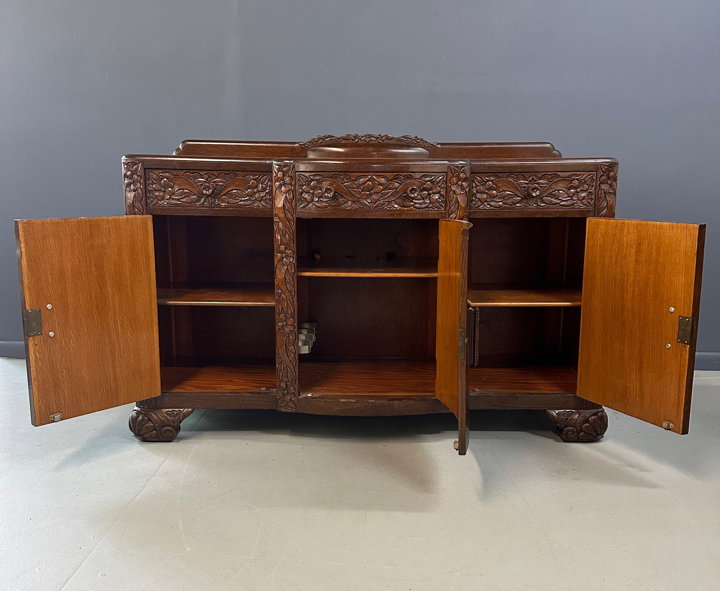 1920s English Art Nouveau sideboard in oak with ornate floral and vine hand-carving, three-door storage, and bun feet