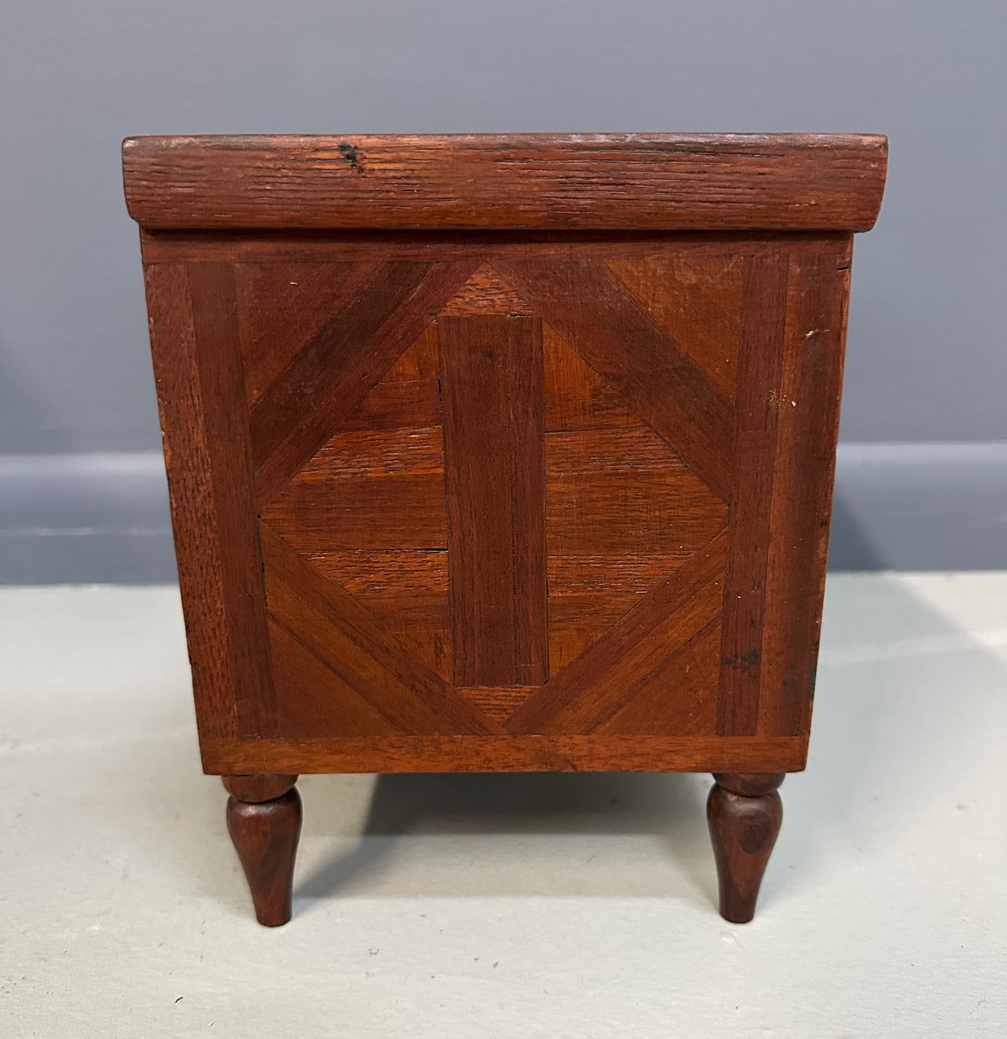 Miniature marquetry blanket chest dated 1910, handcrafted by Flora Boyer of Pennsylvania, featuring intricate geometric inlay patterns in warm-toned wood and a brass keyhole on the front