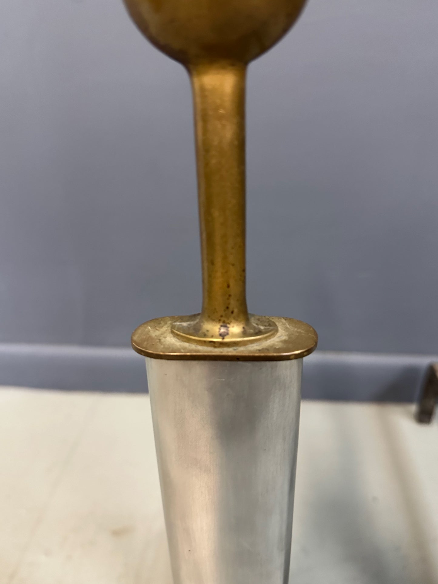 Pair of Machine Age andirons made of polished steel columns with spherical brass finials on top, supported by rugged iron bases with a minimalist, industrial design.