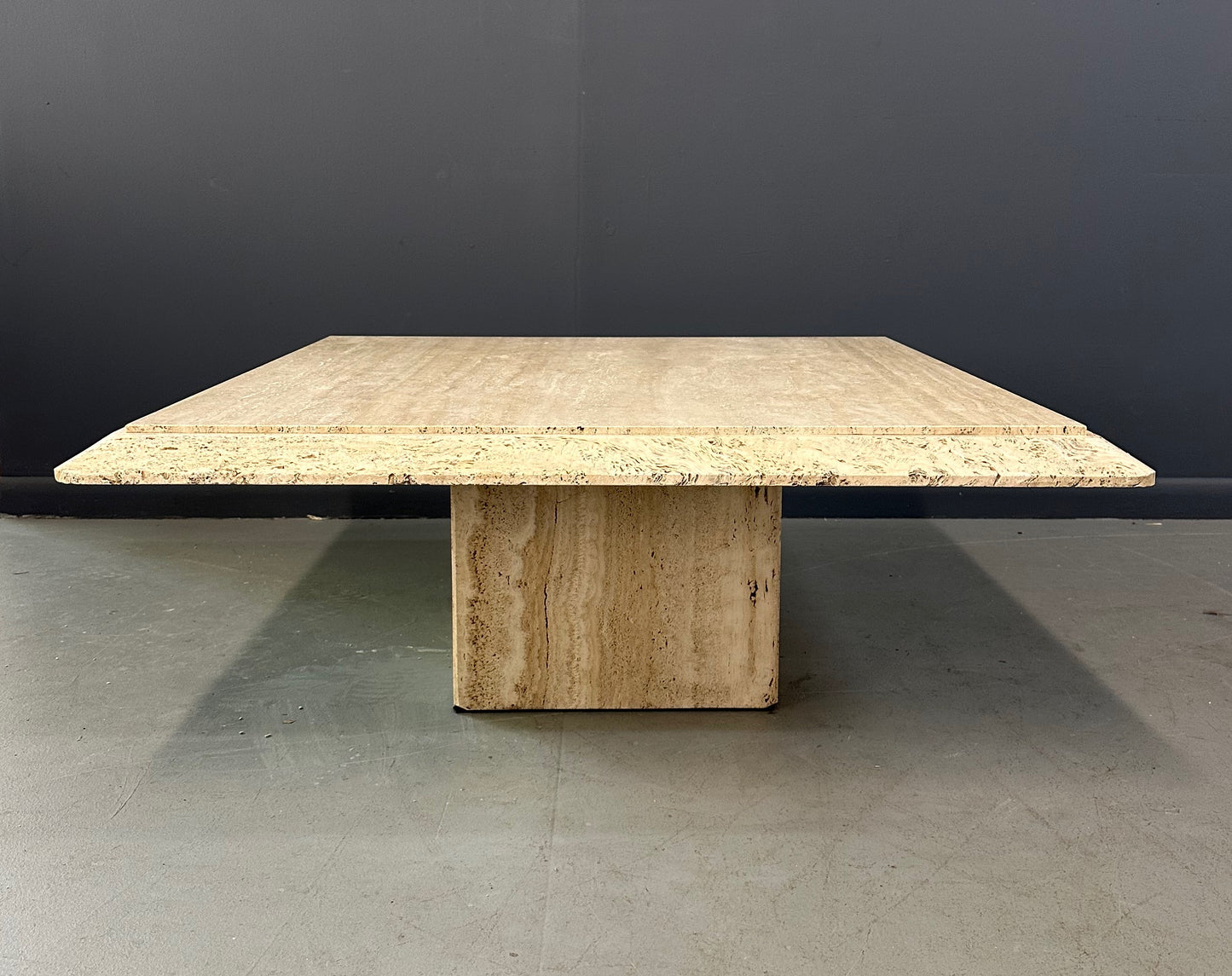 1970s square coffee table crafted from natural travertine stone, featuring a thick slab top with raw, unhoned edges and subtle veining, supported by a sturdy pedestal base for a sculptural, minimalist aesthetic