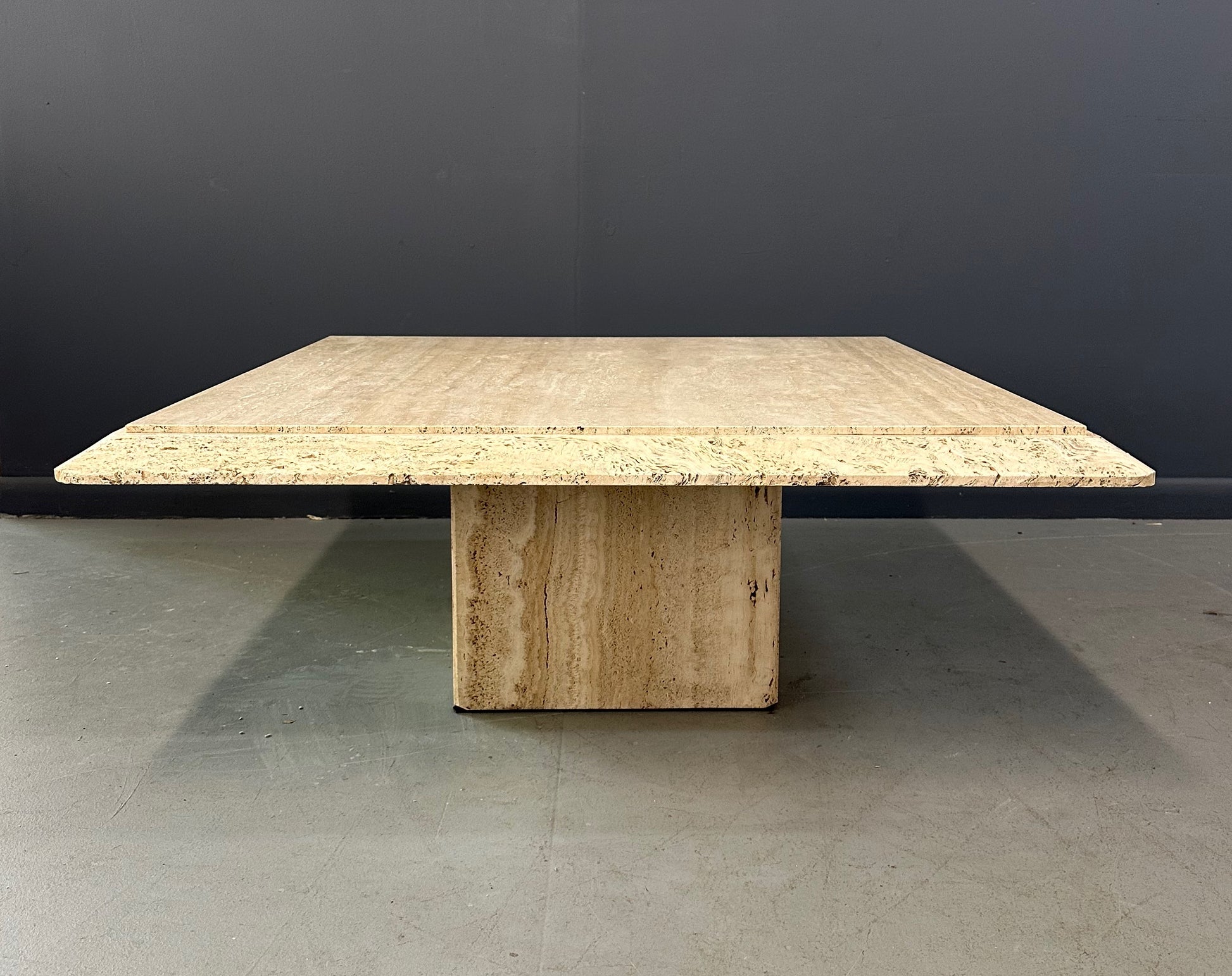 1970s square coffee table crafted from natural travertine stone, featuring a thick slab top with raw, unhoned edges and subtle veining, supported by a sturdy pedestal base for a sculptural, minimalist aesthetic