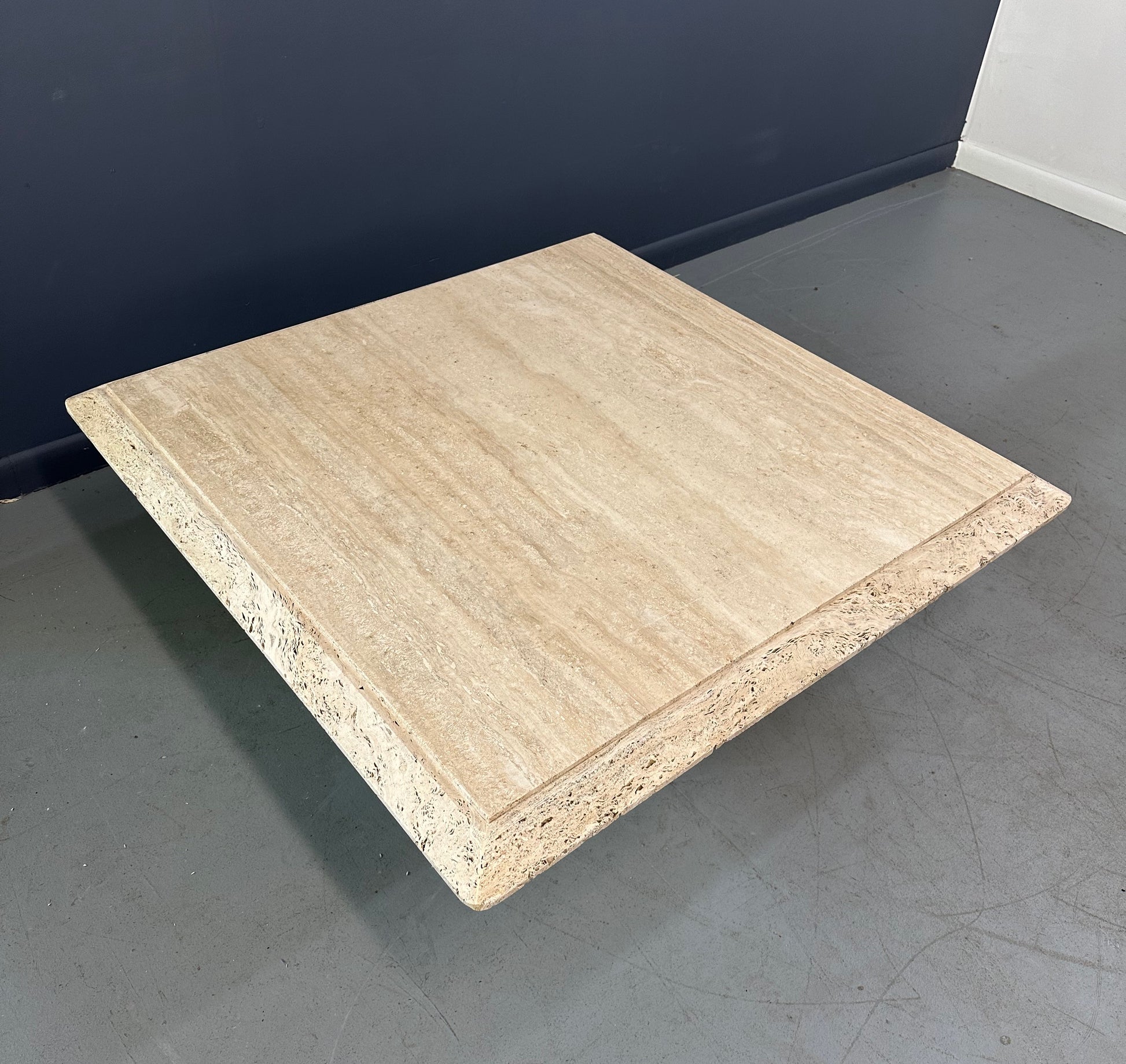 1970s square coffee table crafted from natural travertine stone, featuring a thick slab top with raw, unhoned edges and subtle veining, supported by a sturdy pedestal base for a sculptural, minimalist aesthetic