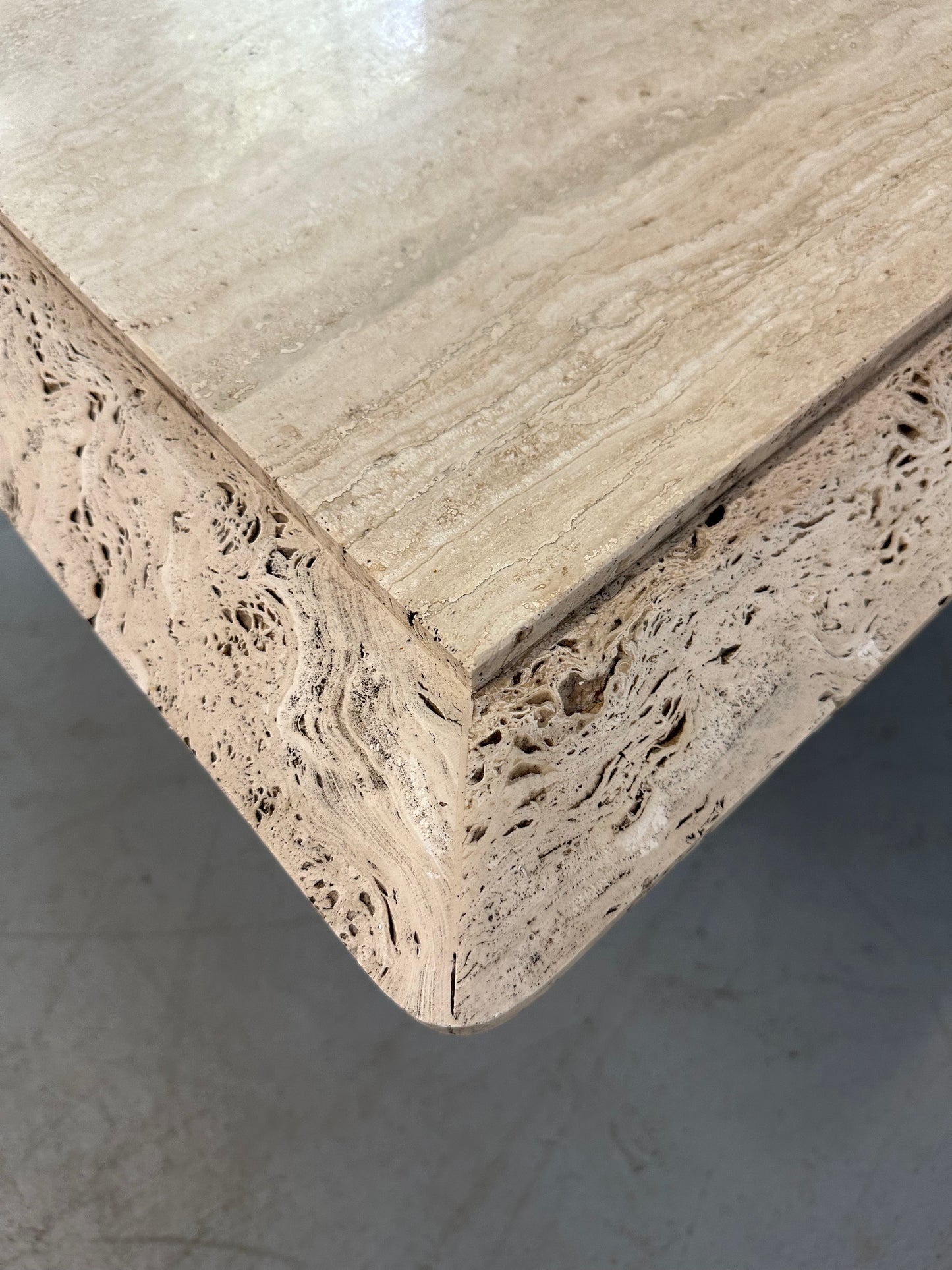 1970s square coffee table crafted from natural travertine stone, featuring a thick slab top with raw, unhoned edges and subtle veining, supported by a sturdy pedestal base for a sculptural, minimalist aesthetic