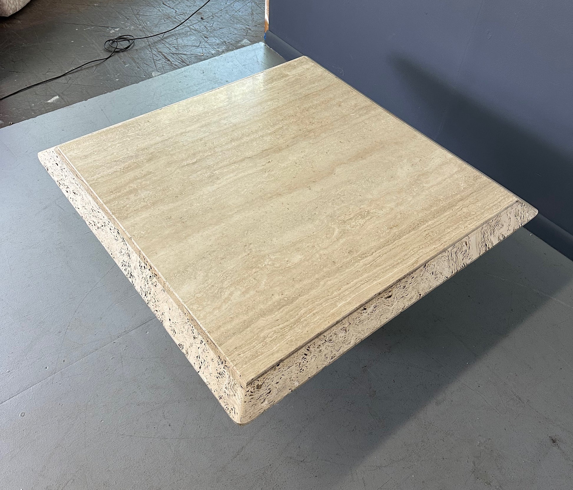 1970s square coffee table crafted from natural travertine stone, featuring a thick slab top with raw, unhoned edges and subtle veining, supported by a sturdy pedestal base for a sculptural, minimalist aesthetic