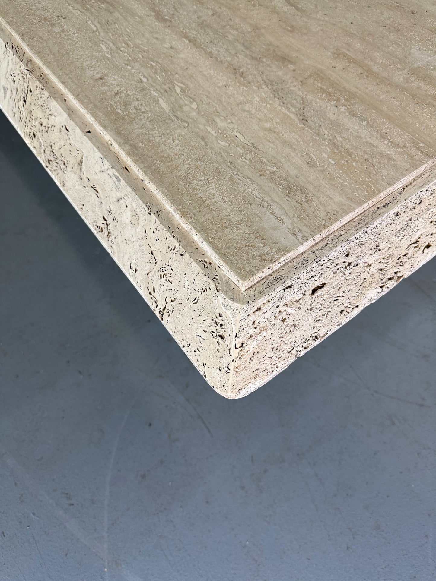 1970s square coffee table crafted from natural travertine stone, featuring a thick slab top with raw, unhoned edges and subtle veining, supported by a sturdy pedestal base for a sculptural, minimalist aesthetic