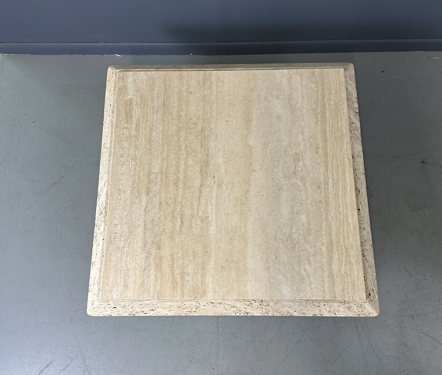 1970s square coffee table crafted from natural travertine stone, featuring a thick slab top with raw, unhoned edges and subtle veining, supported by a sturdy pedestal base for a sculptural, minimalist aesthetic