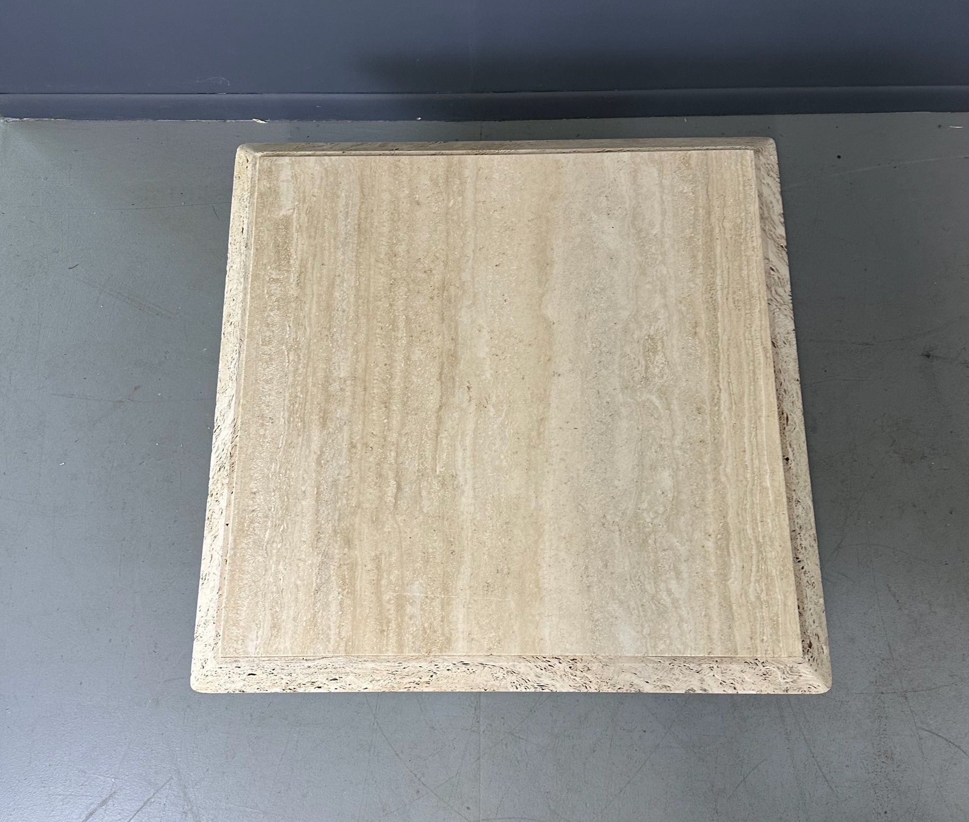 1970s square coffee table crafted from natural travertine stone, featuring a thick slab top with raw, unhoned edges and subtle veining, supported by a sturdy pedestal base for a sculptural, minimalist aesthetic