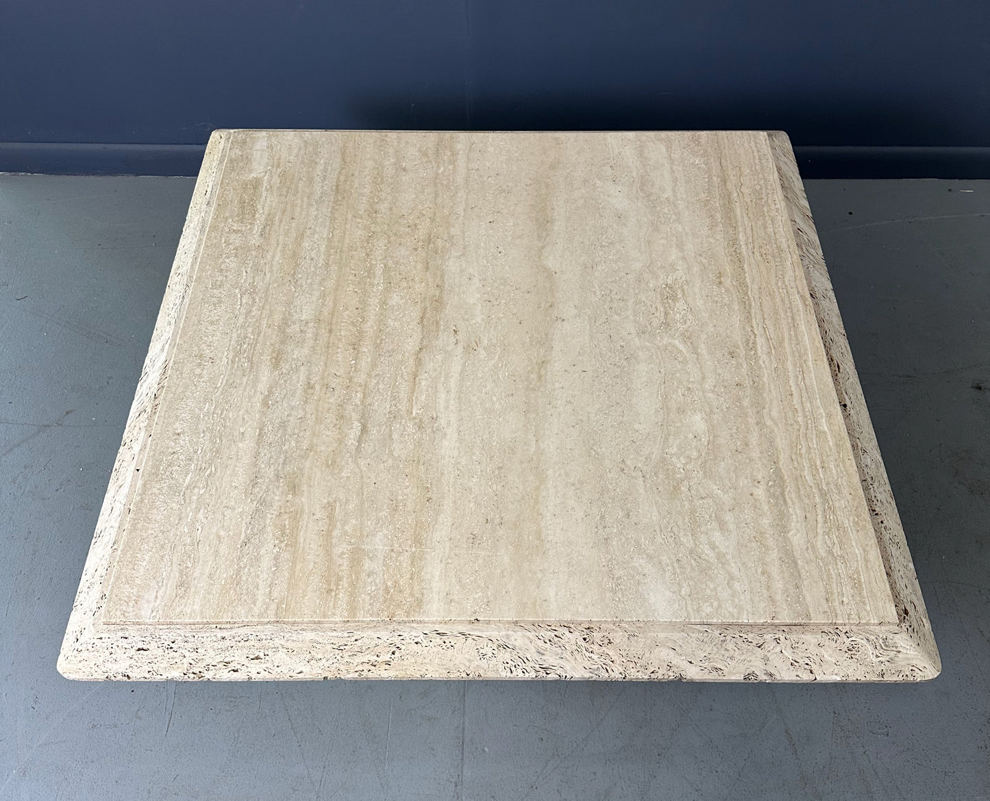1970s square coffee table crafted from natural travertine stone, featuring a thick slab top with raw, unhoned edges and subtle veining, supported by a sturdy pedestal base for a sculptural, minimalist aesthetic