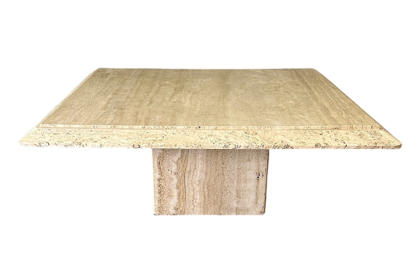 1970s square coffee table crafted from natural travertine stone, featuring a thick slab top with raw, unhoned edges and subtle veining, supported by a sturdy pedestal base for a sculptural, minimalist aesthetic