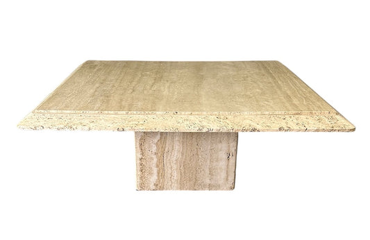1970s square coffee table crafted from natural travertine stone, featuring a thick slab top with raw, unhoned edges and subtle veining, supported by a sturdy pedestal base for a sculptural, minimalist aesthetic
