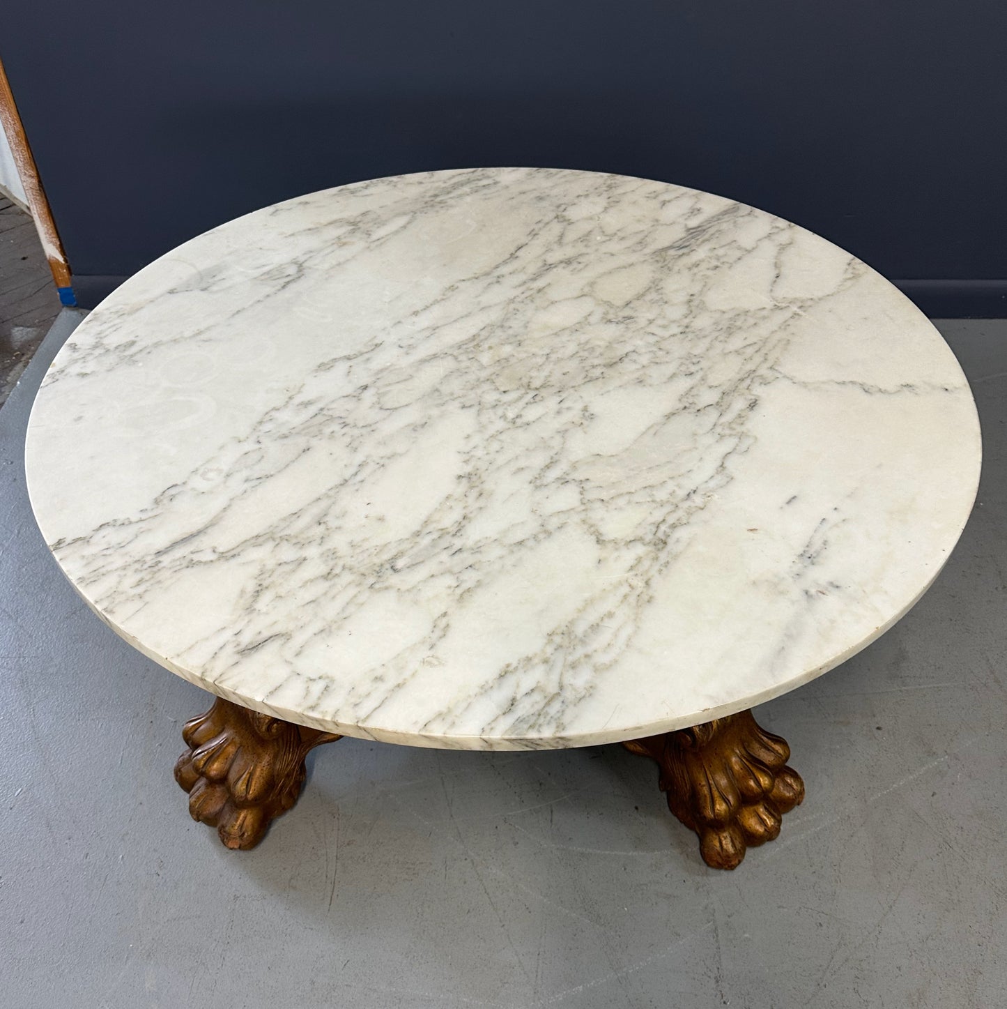 20th-century Empire-style Hollywood Regency coffee table featuring a round white marble top with elegant gray veining, supported by a gilded wood base with bold lion paw feet and neoclassical design elements