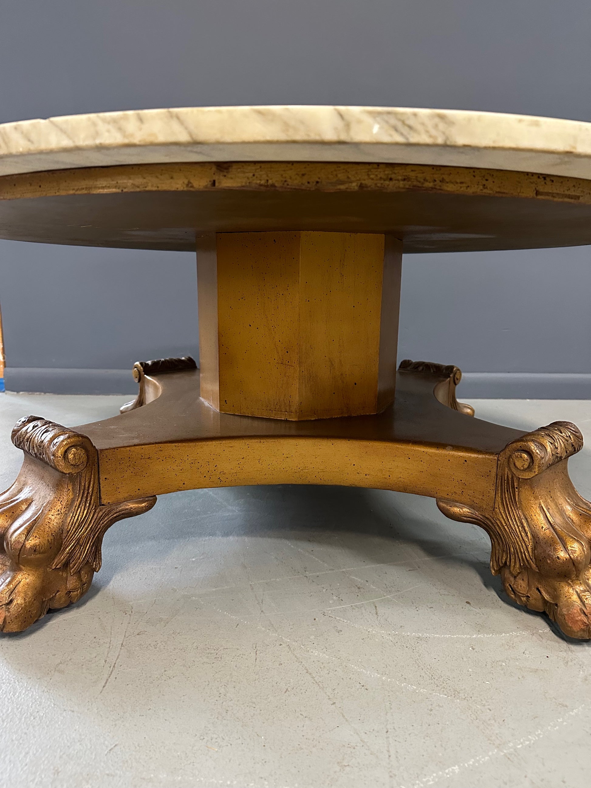 20th-century Empire-style Hollywood Regency coffee table featuring a round white marble top with elegant gray veining, supported by a gilded wood base with bold lion paw feet and neoclassical design elements
