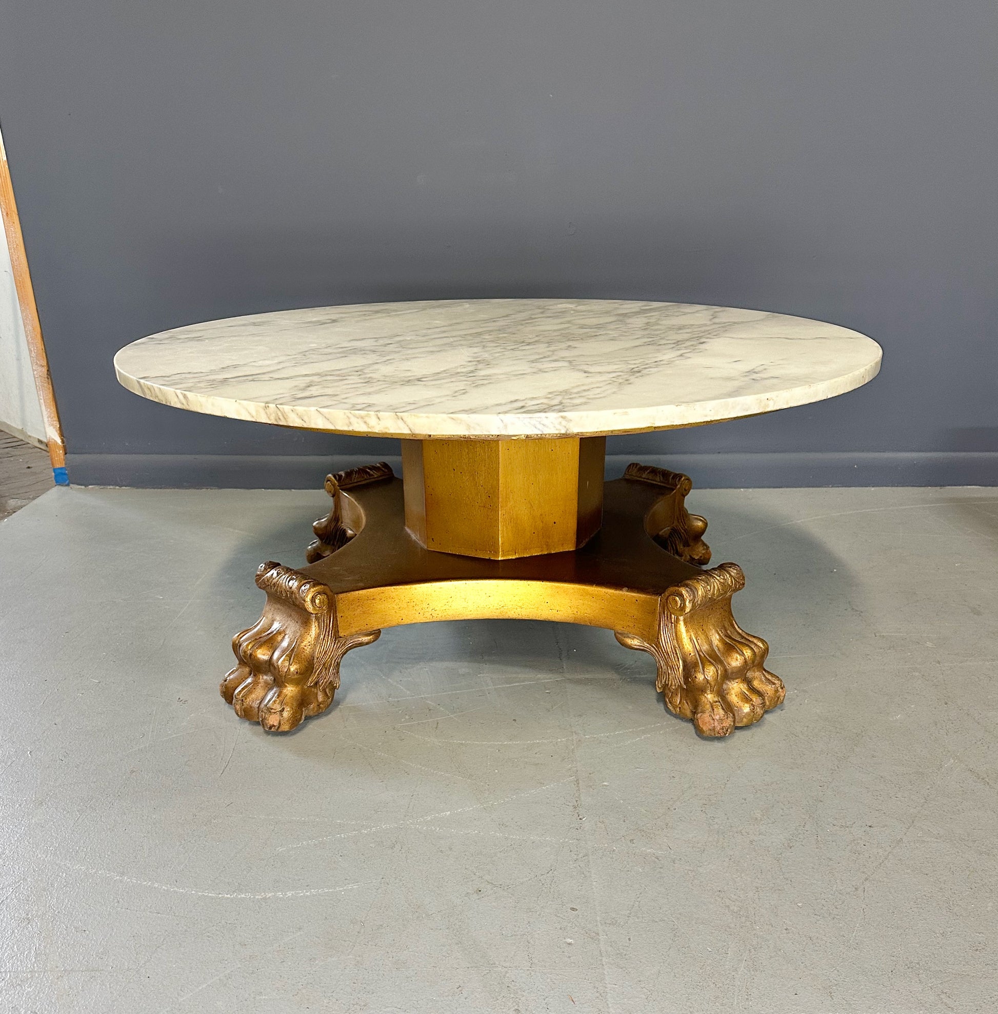 20th-century Empire-style Hollywood Regency coffee table featuring a round white marble top with elegant gray veining, supported by a gilded wood base with bold lion paw feet and neoclassical design elements