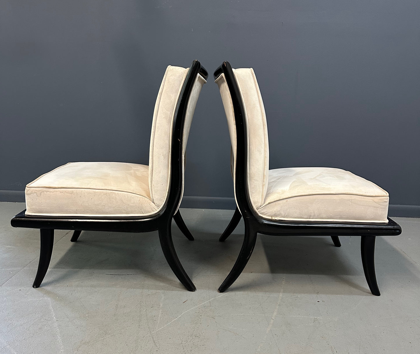 Pair of mid-century modern slipper chairs with ebonized wood frames and cream velvet upholstery, designed in the style of Robsjohn-Gibbings, featuring elegant curves and tapered legs