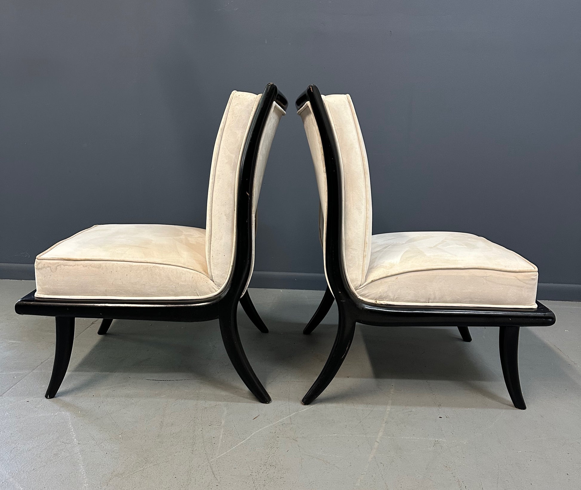 Pair of mid-century modern slipper chairs with ebonized wood frames and cream velvet upholstery, designed in the style of Robsjohn-Gibbings, featuring elegant curves and tapered legs