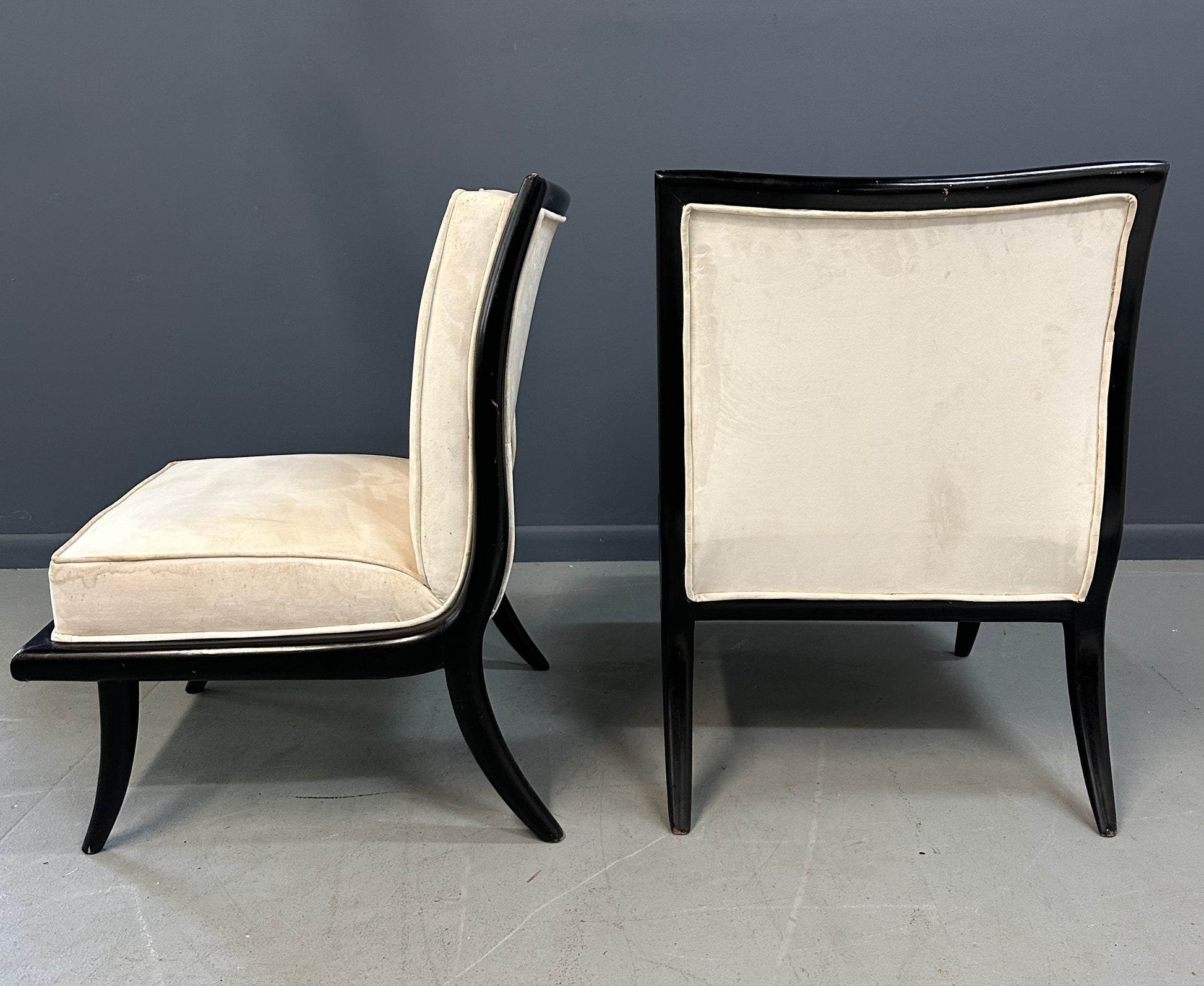Pair of mid-century modern slipper chairs with ebonized wood frames and cream velvet upholstery, designed in the style of Robsjohn-Gibbings, featuring elegant curves and tapered legs