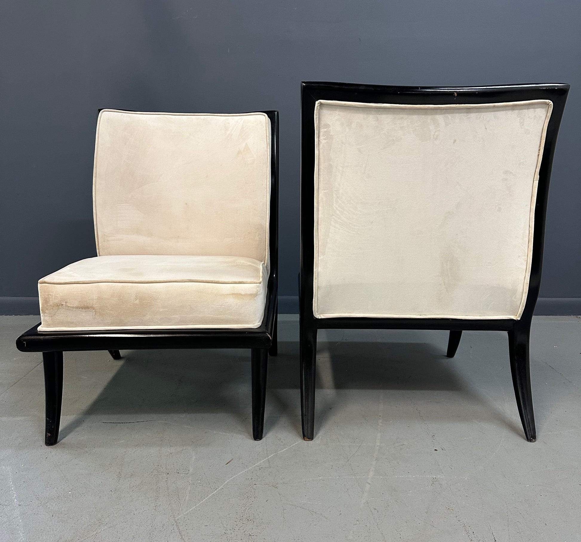 Pair of mid-century modern slipper chairs with ebonized wood frames and cream velvet upholstery, designed in the style of Robsjohn-Gibbings, featuring elegant curves and tapered legs