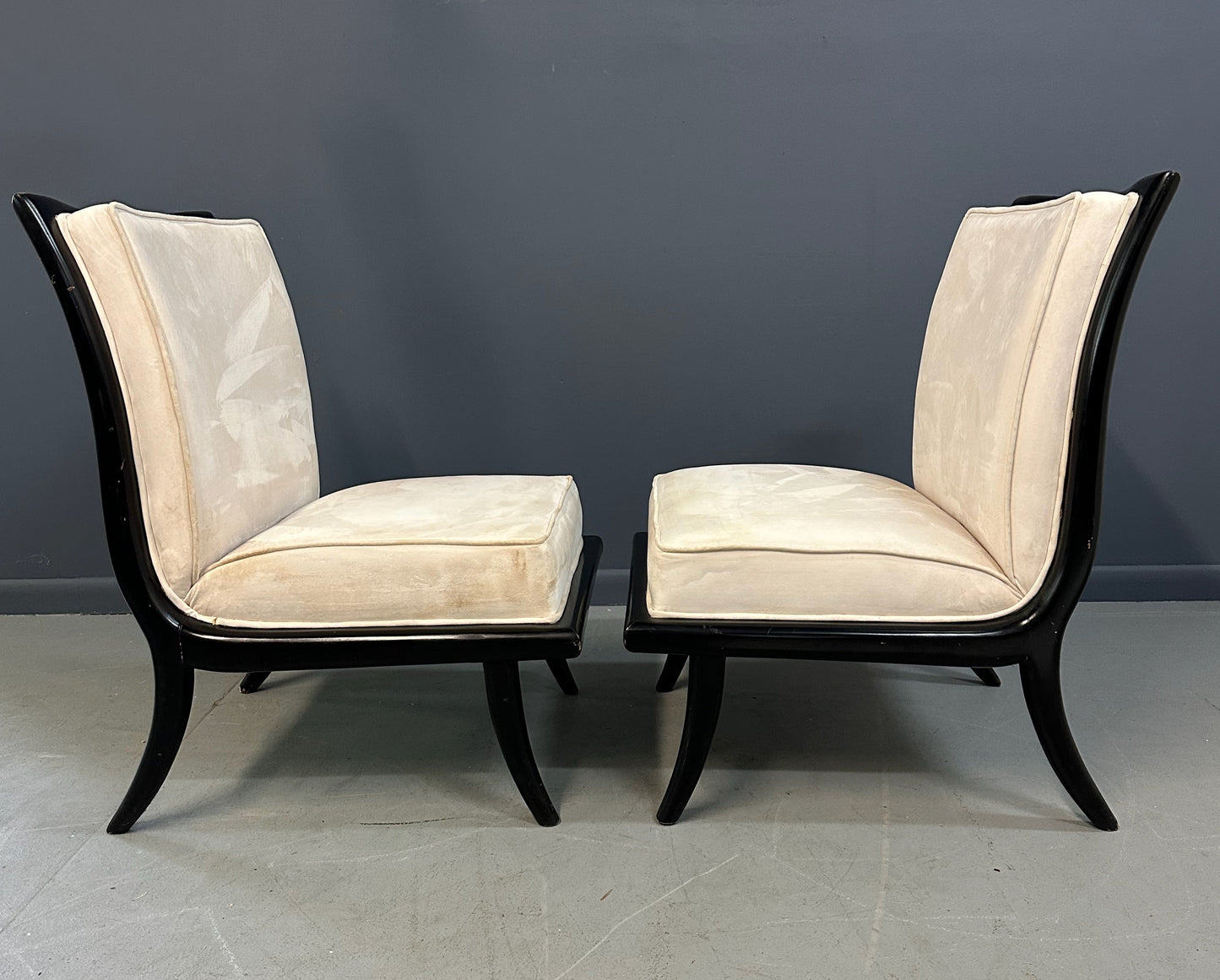 Pair of mid-century modern slipper chairs with ebonized wood frames and cream velvet upholstery, designed in the style of Robsjohn-Gibbings, featuring elegant curves and tapered legs