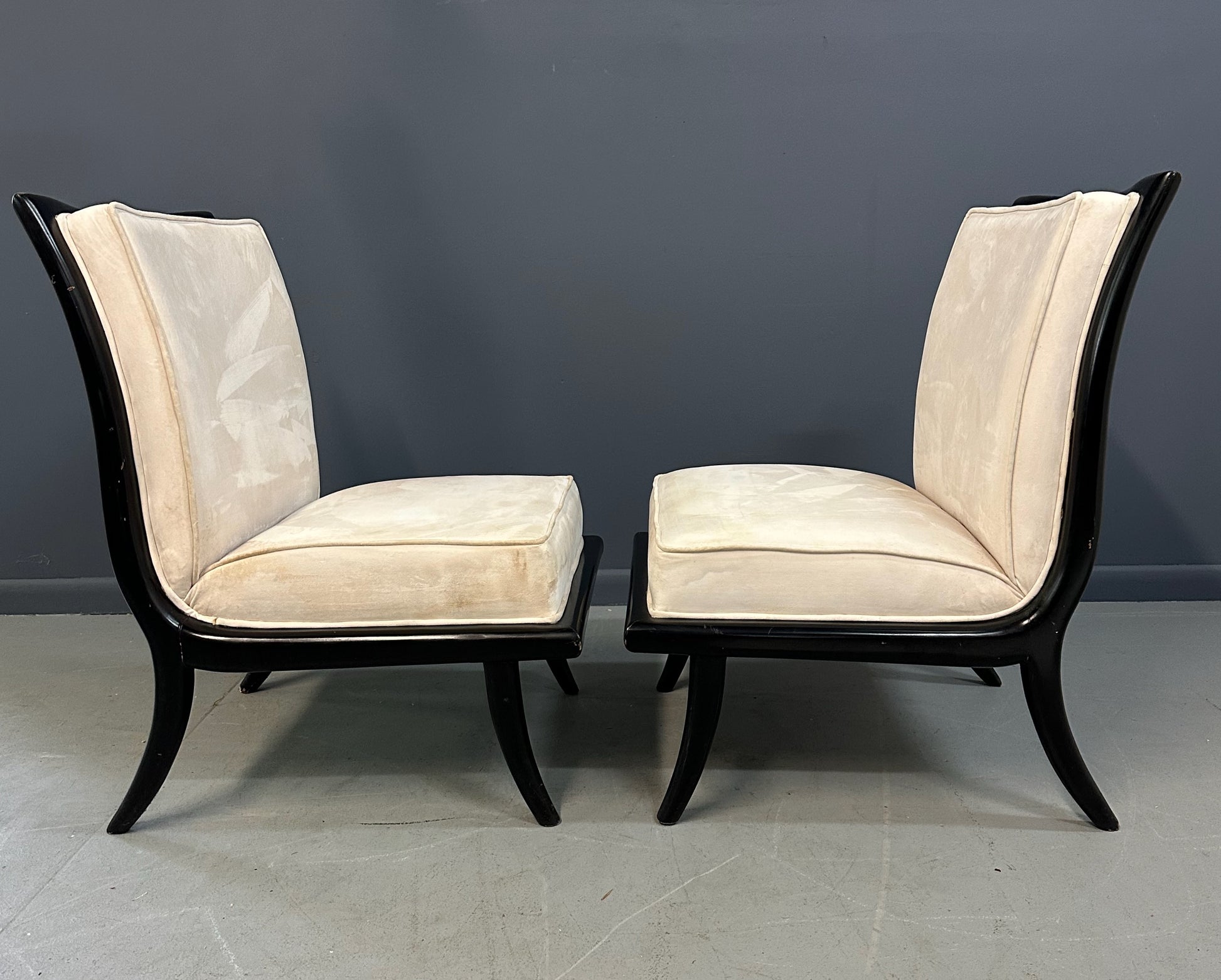 Pair of mid-century modern slipper chairs with ebonized wood frames and cream velvet upholstery, designed in the style of Robsjohn-Gibbings, featuring elegant curves and tapered legs