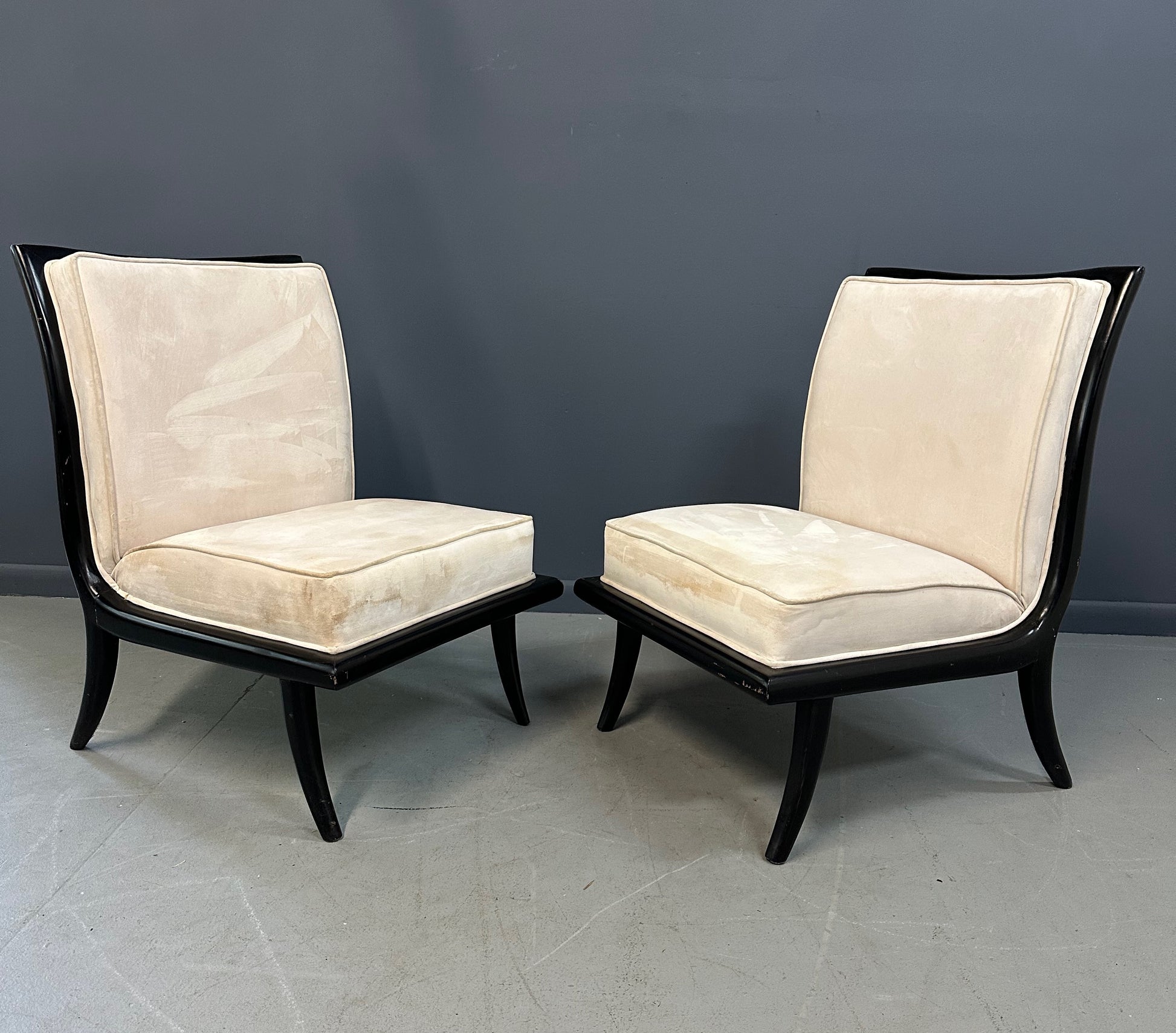Pair of mid-century modern slipper chairs with ebonized wood frames and cream velvet upholstery, designed in the style of Robsjohn-Gibbings, featuring elegant curves and tapered legs