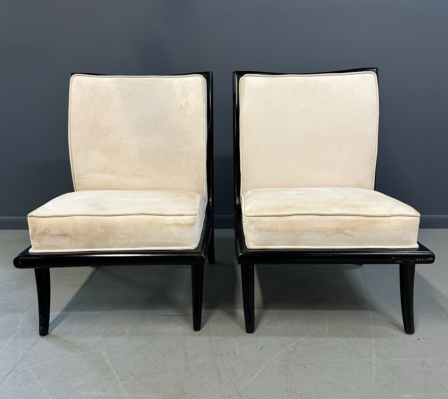 Pair of mid-century modern slipper chairs with ebonized wood frames and cream velvet upholstery, designed in the style of Robsjohn-Gibbings, featuring elegant curves and tapered legs