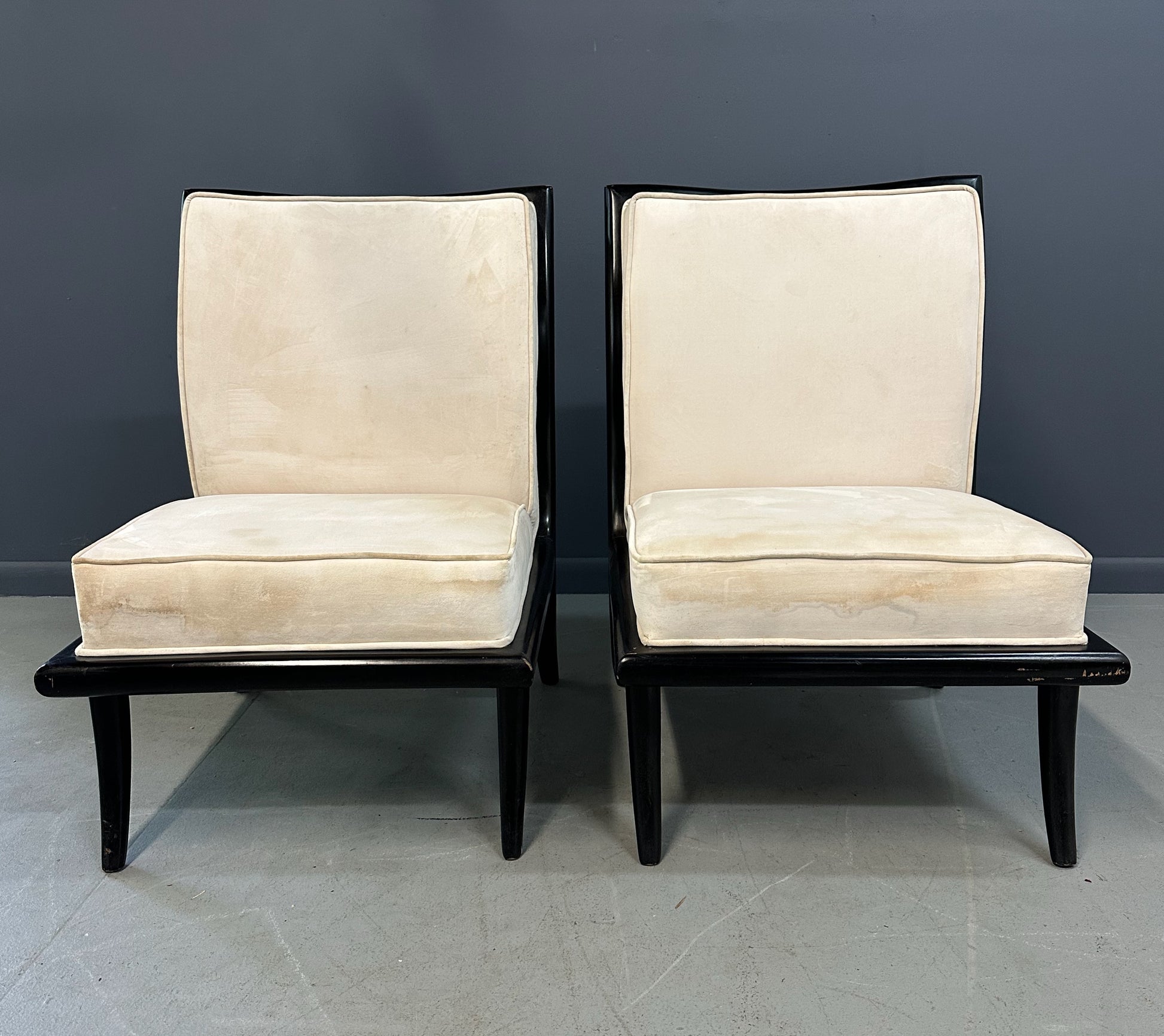 Pair of mid-century modern slipper chairs with ebonized wood frames and cream velvet upholstery, designed in the style of Robsjohn-Gibbings, featuring elegant curves and tapered legs