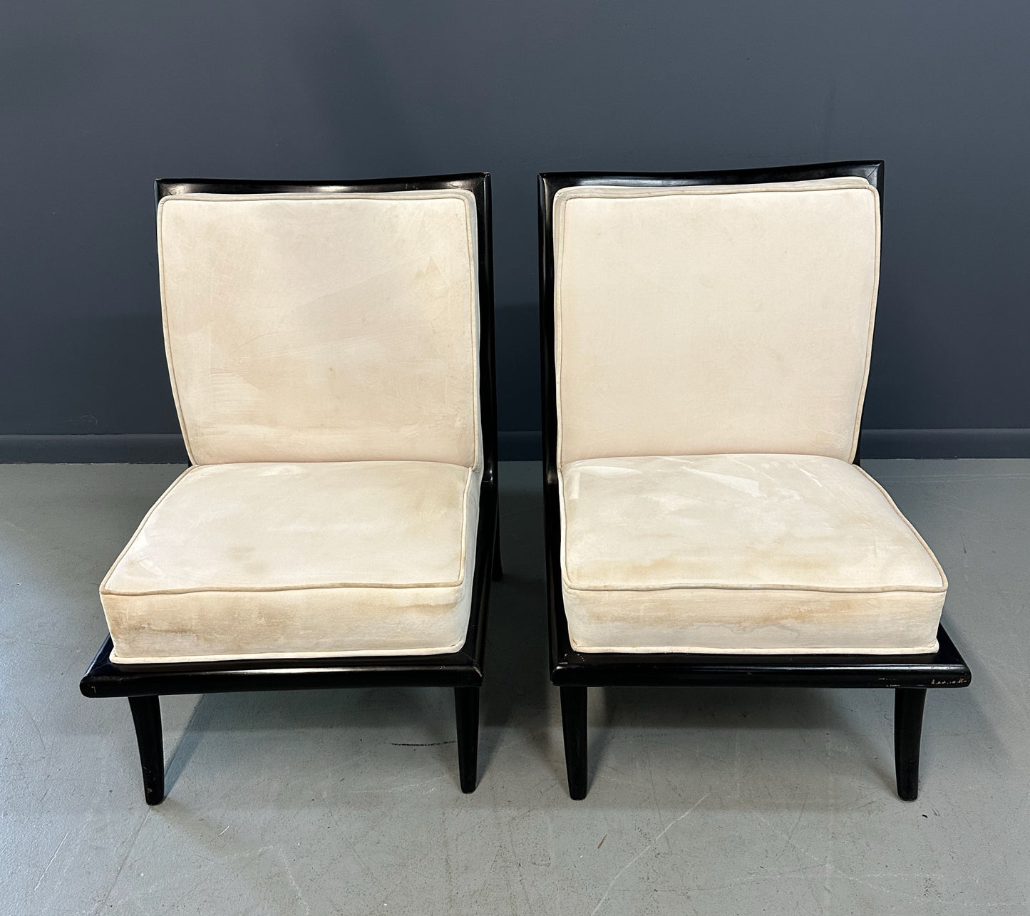 Pair of mid-century modern slipper chairs with ebonized wood frames and cream velvet upholstery, designed in the style of Robsjohn-Gibbings, featuring elegant curves and tapered legs