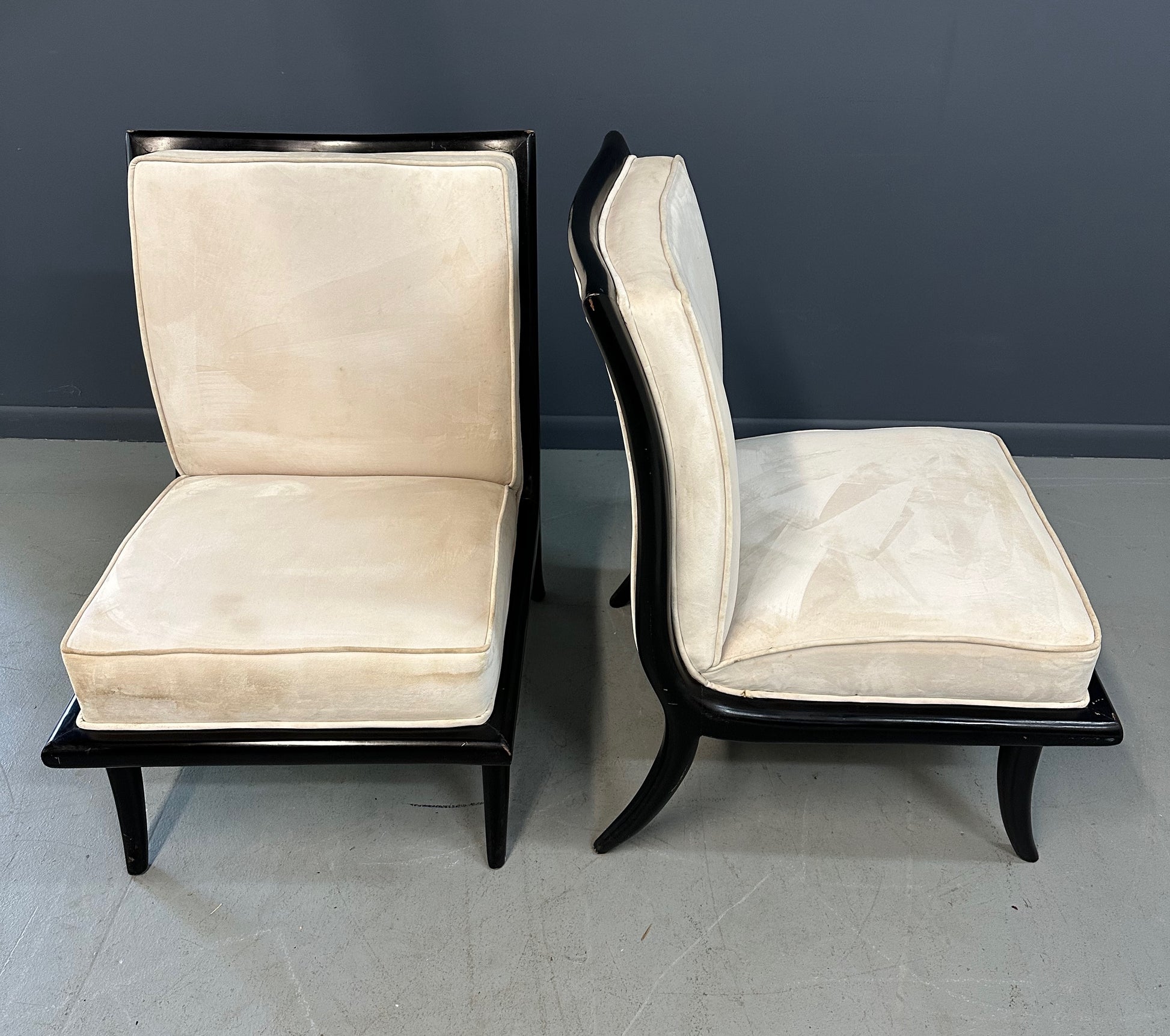 Pair of mid-century modern slipper chairs with ebonized wood frames and cream velvet upholstery, designed in the style of Robsjohn-Gibbings, featuring elegant curves and tapered legs