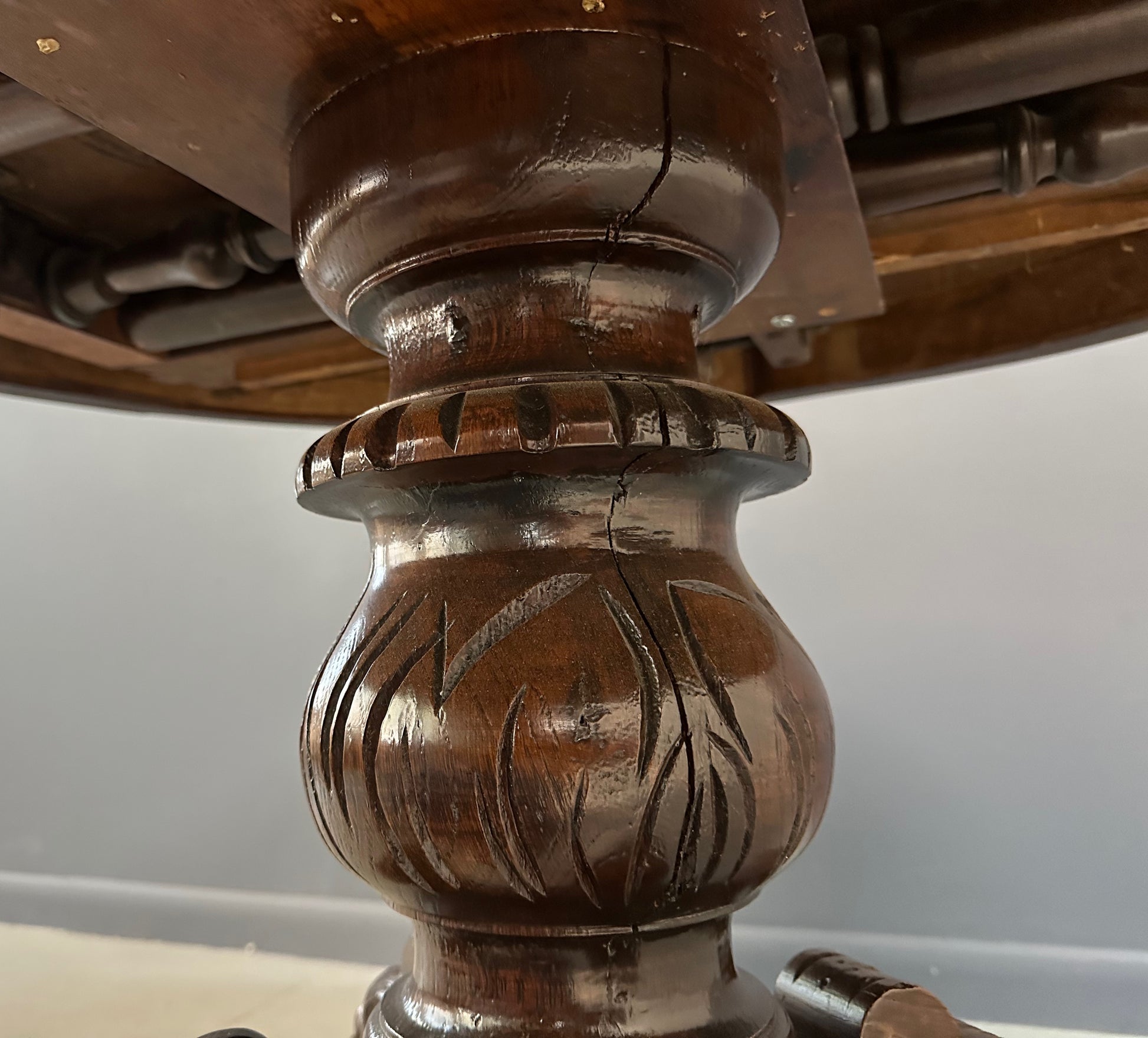 Antique French early 1900s round dining table crafted in rich fruitwood with a carved apron and an intricately detailed pedestal base featuring scrollwork and foliage motifs
