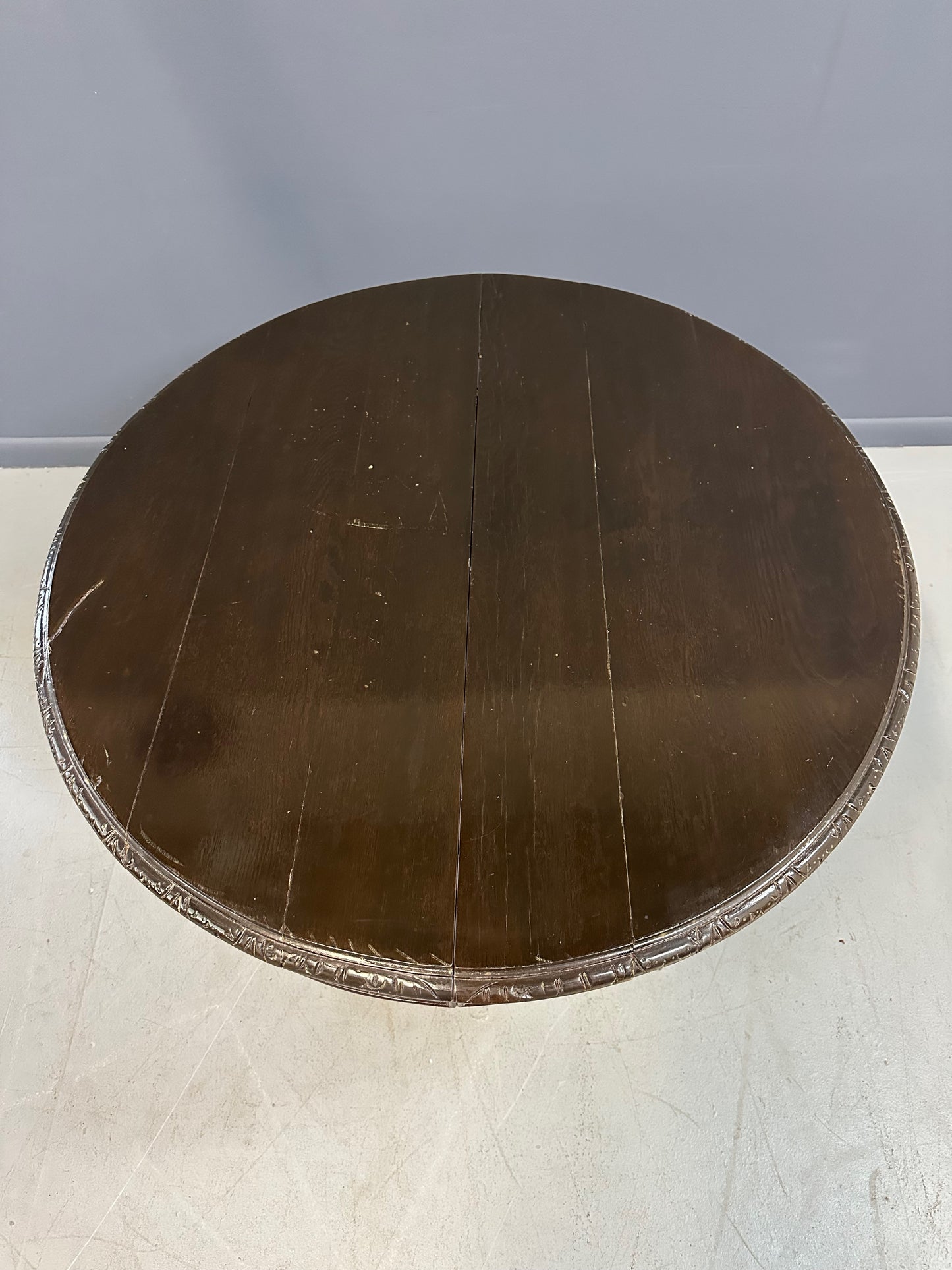 Antique French early 1900s round dining table crafted in rich fruitwood with a carved apron and an intricately detailed pedestal base featuring scrollwork and foliage motifs
