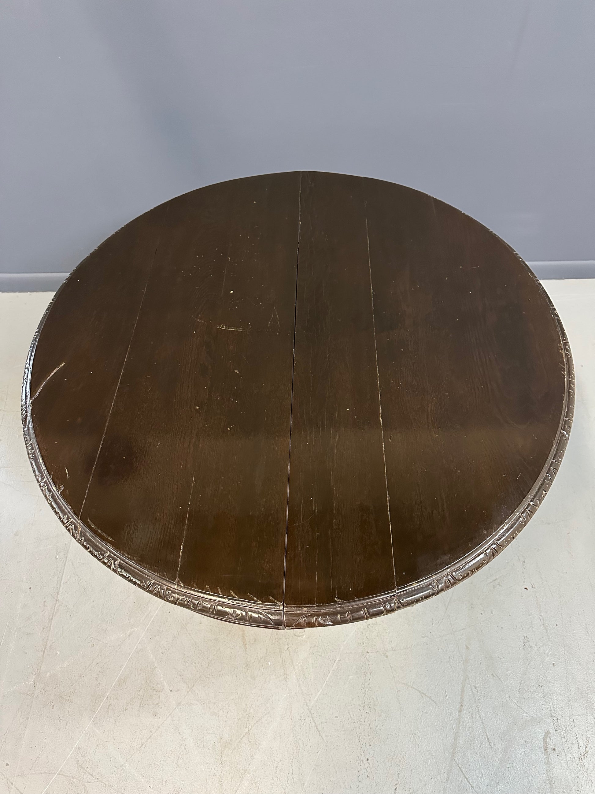 Antique French early 1900s round dining table crafted in rich fruitwood with a carved apron and an intricately detailed pedestal base featuring scrollwork and foliage motifs