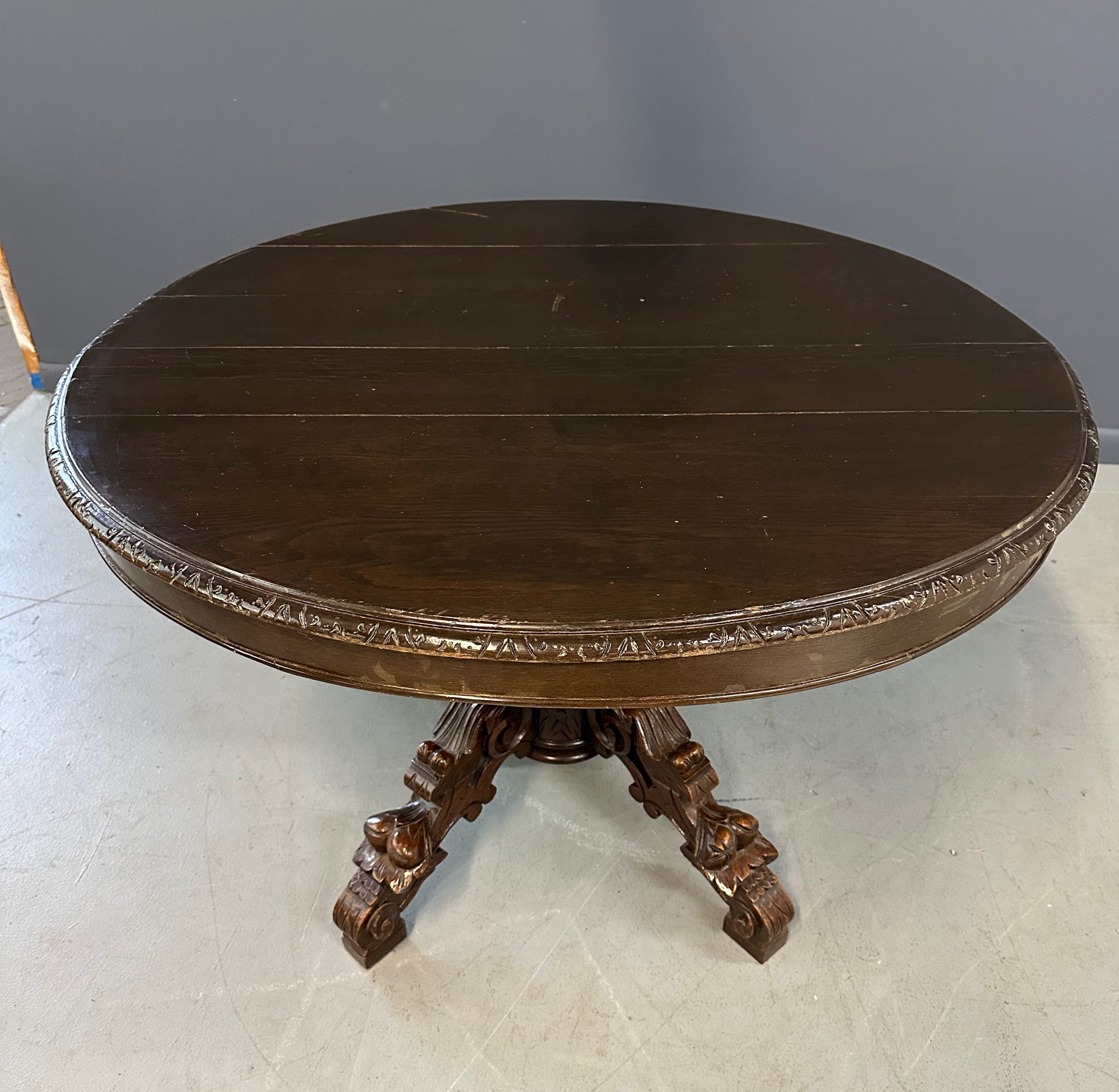 Antique French early 1900s round dining table crafted in rich fruitwood with a carved apron and an intricately detailed pedestal base featuring scrollwork and foliage motifs