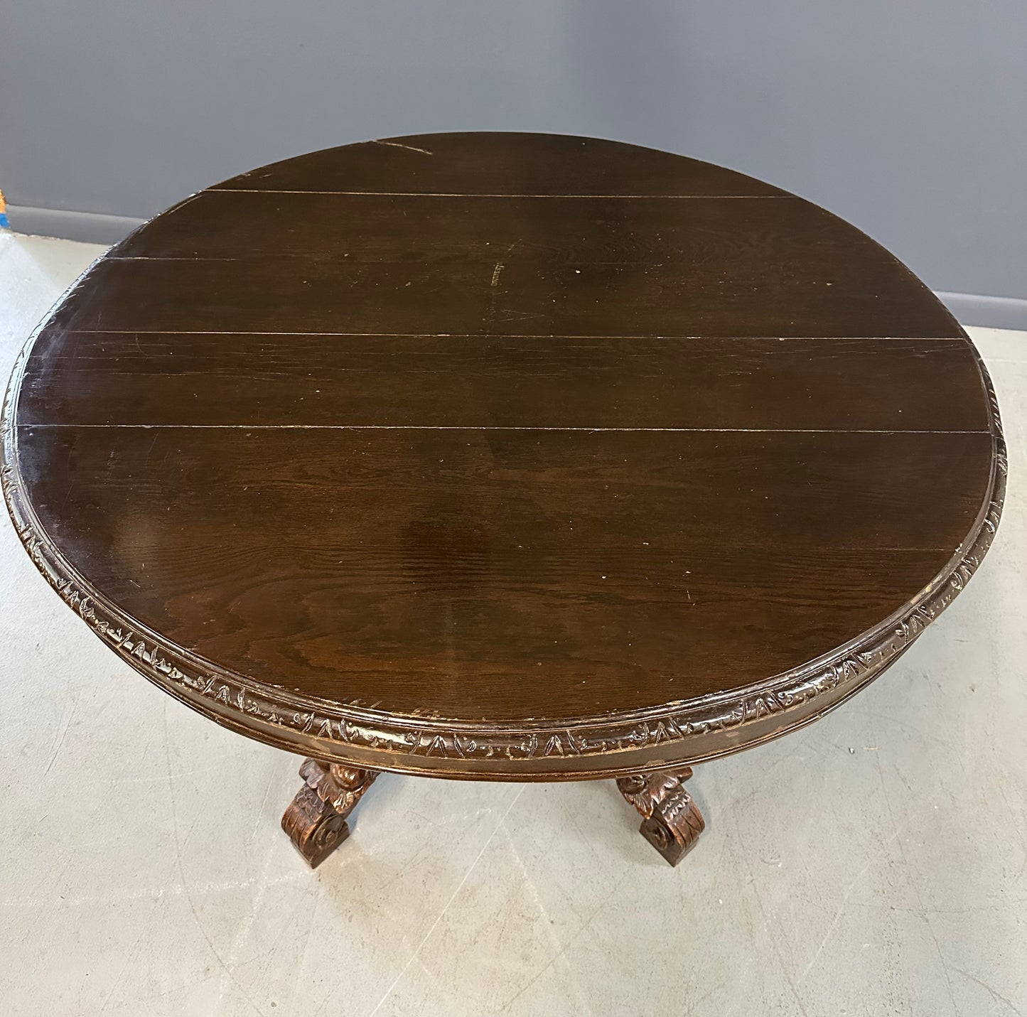 Antique French early 1900s round dining table crafted in rich fruitwood with a carved apron and an intricately detailed pedestal base featuring scrollwork and foliage motifs