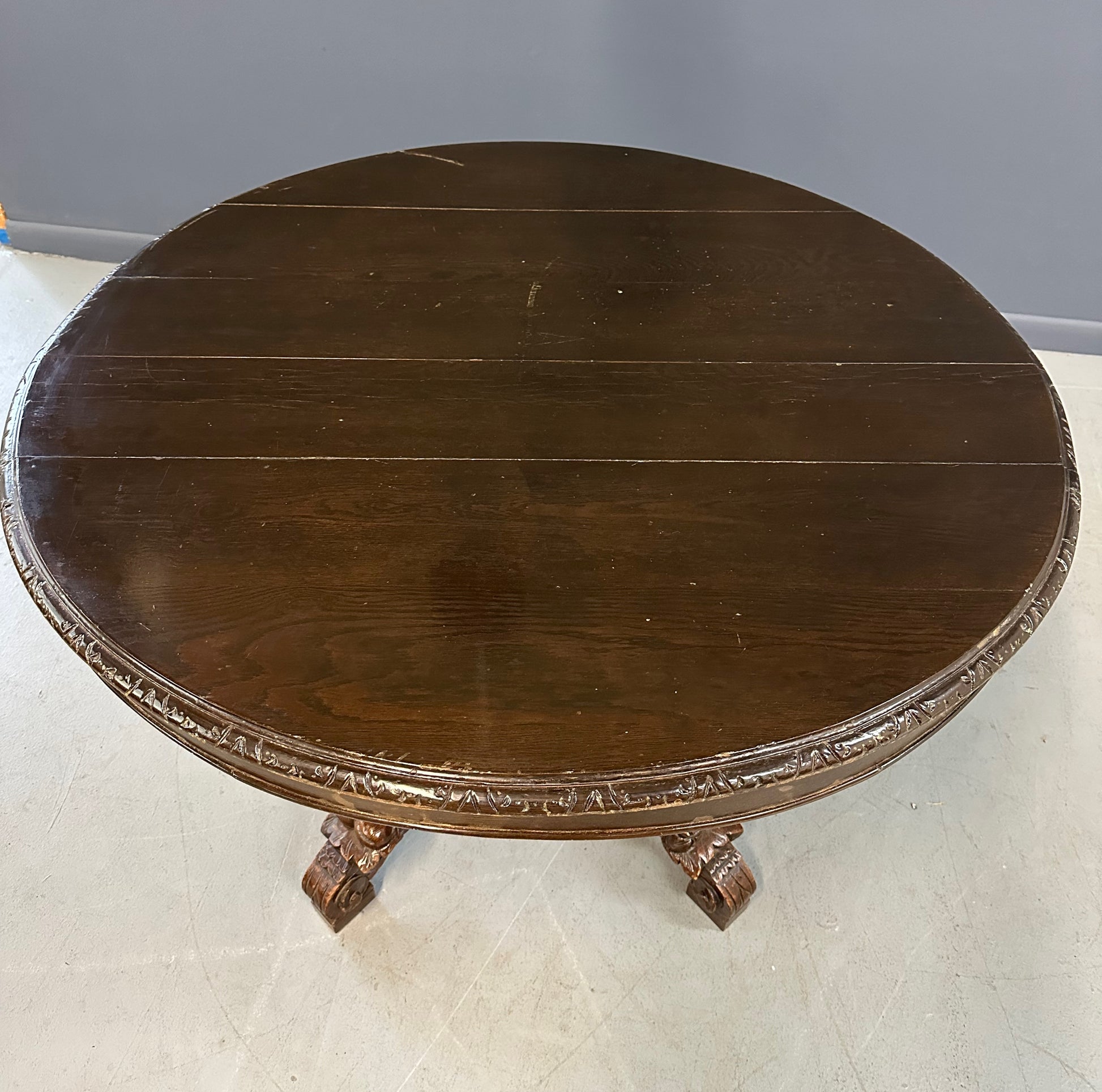 Antique French early 1900s round dining table crafted in rich fruitwood with a carved apron and an intricately detailed pedestal base featuring scrollwork and foliage motifs