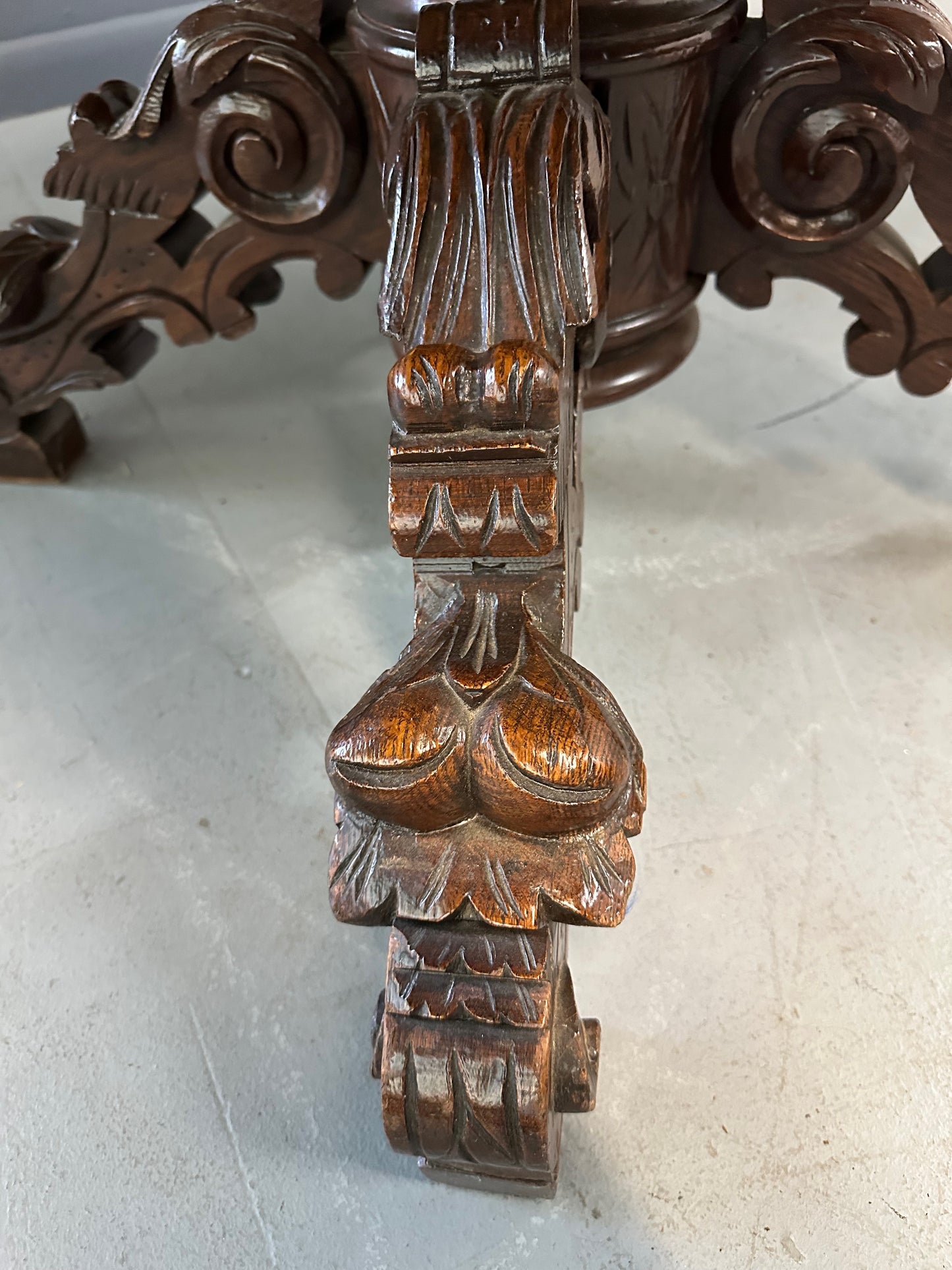 Antique French early 1900s round dining table crafted in rich fruitwood with a carved apron and an intricately detailed pedestal base featuring scrollwork and foliage motifs