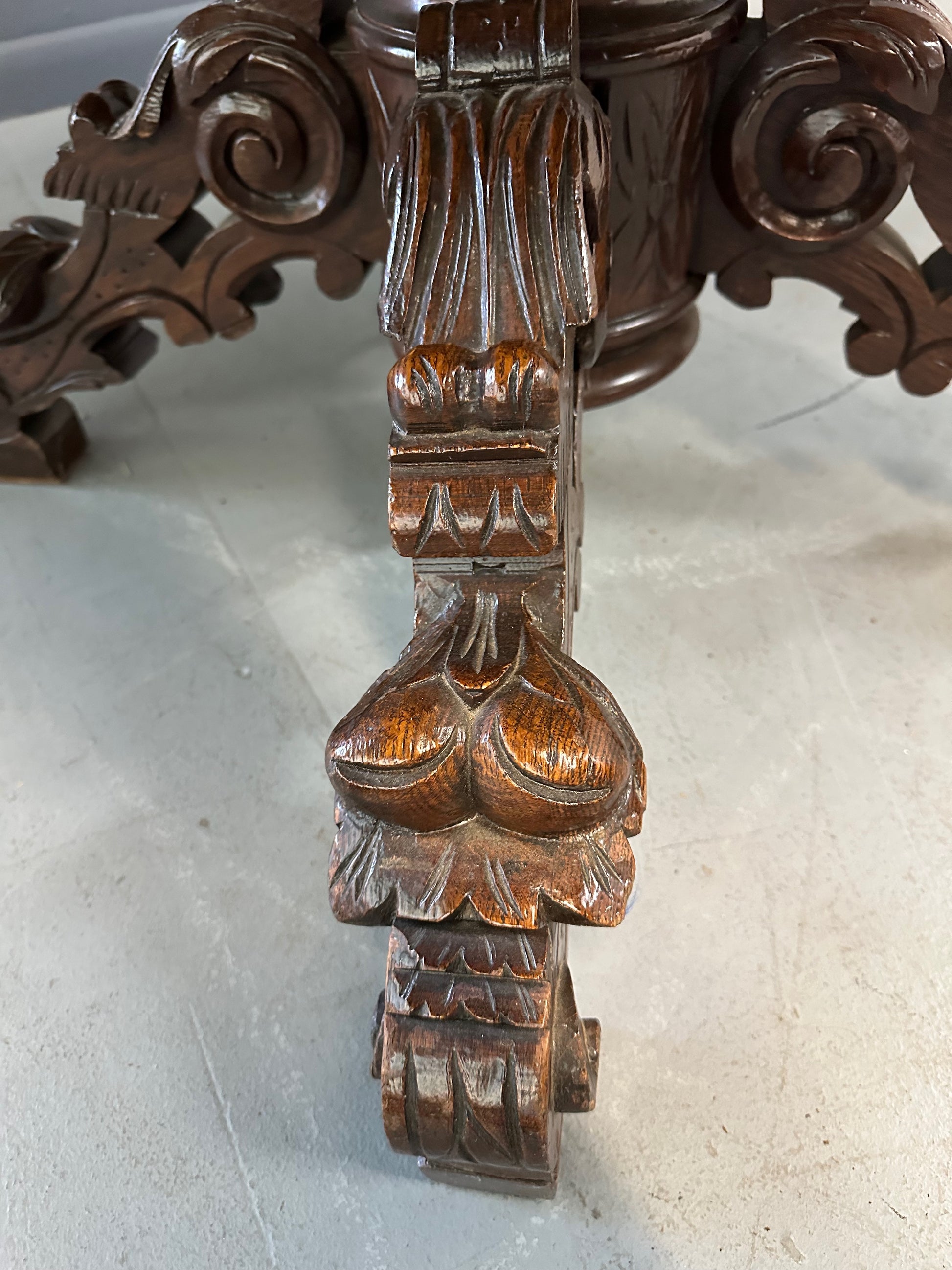 Antique French early 1900s round dining table crafted in rich fruitwood with a carved apron and an intricately detailed pedestal base featuring scrollwork and foliage motifs