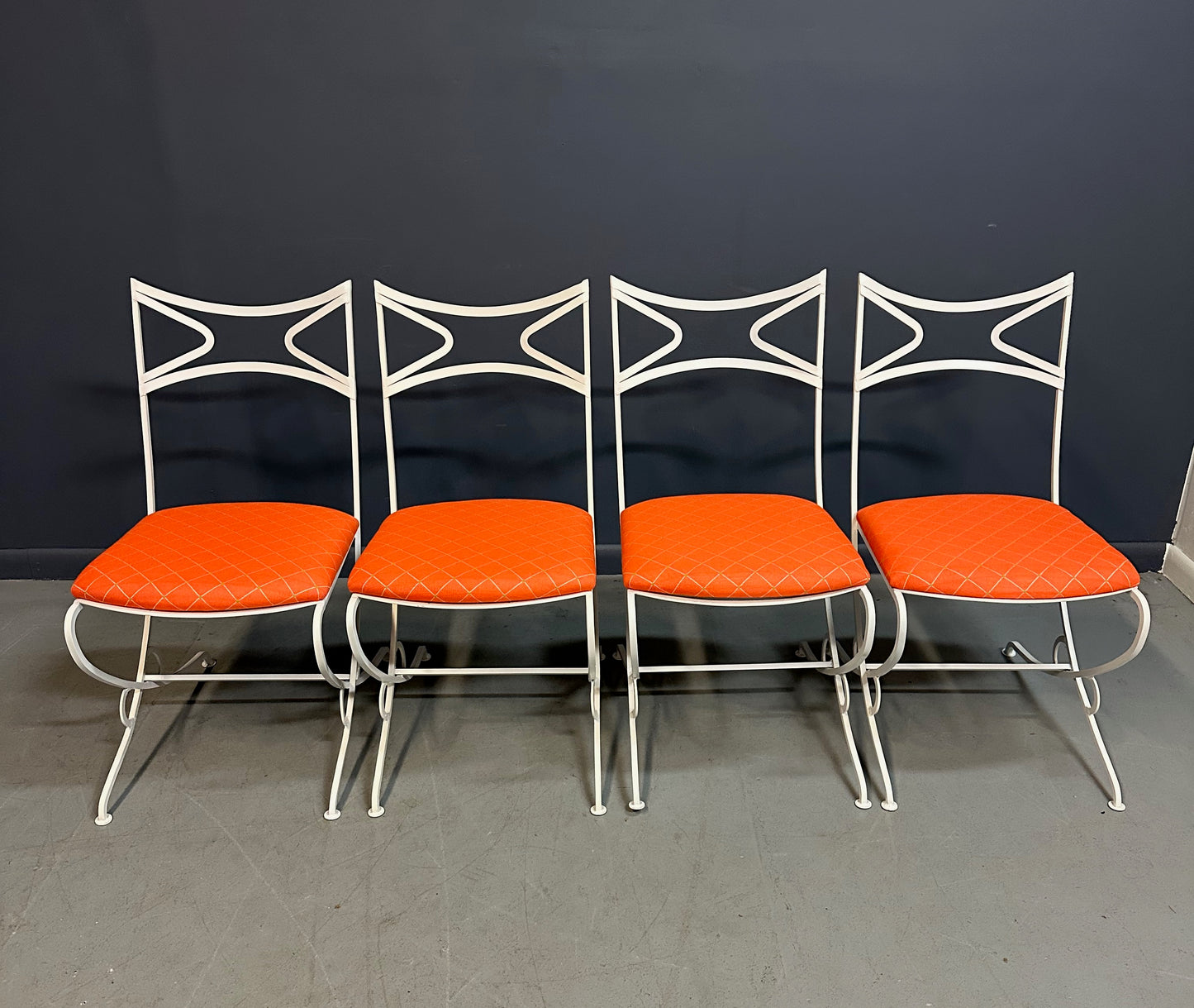 1940s French mid-century modern outdoor dining set featuring six white wrought iron chairs with orange diamond-patterned cushions and a matching table with decorative curved frames