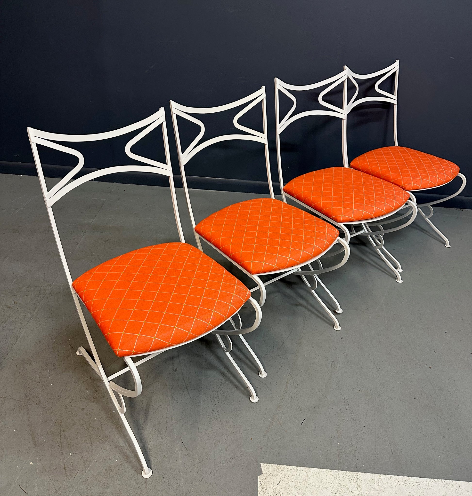 1940s French mid-century modern outdoor dining set featuring six white wrought iron chairs with orange diamond-patterned cushions and a matching table with decorative curved frames