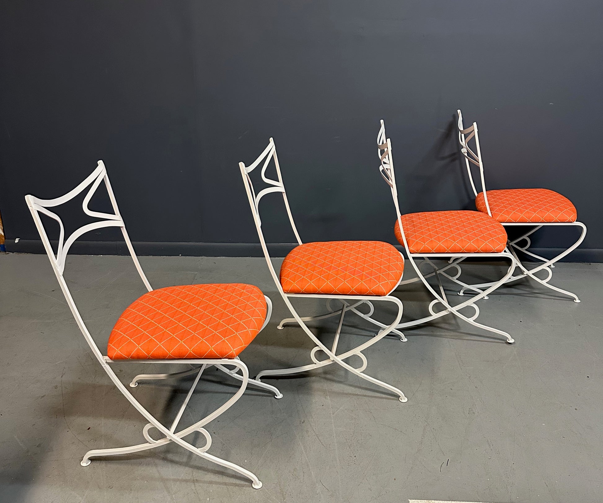 1940s French mid-century modern outdoor dining set featuring six white wrought iron chairs with orange diamond-patterned cushions and a matching table with decorative curved frames