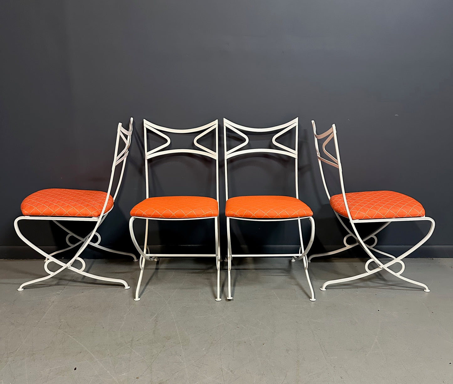 1940s French mid-century modern outdoor dining set featuring six white wrought iron chairs with orange diamond-patterned cushions and a matching table with decorative curved frames