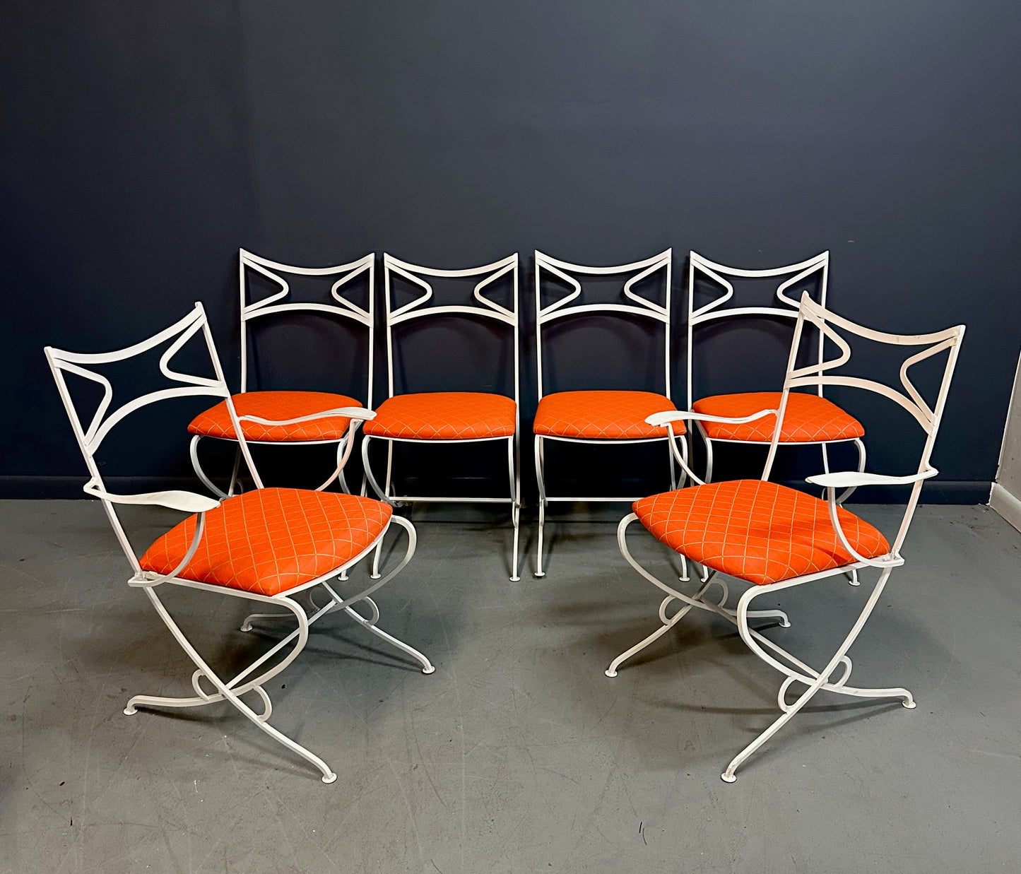 1940s French mid-century modern outdoor dining set featuring six white wrought iron chairs with orange diamond-patterned cushions and a matching table with decorative curved frames