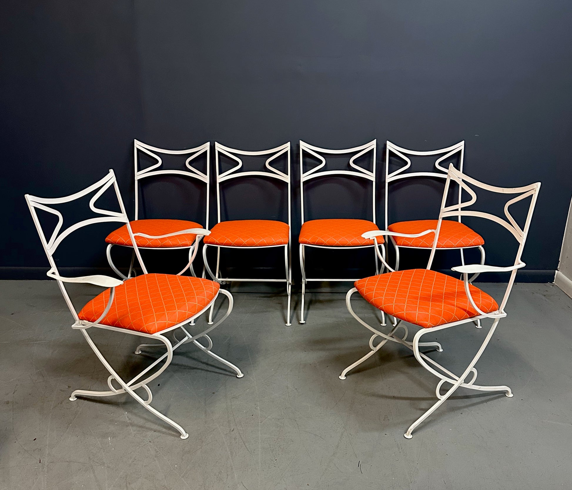 1940s French mid-century modern outdoor dining set featuring six white wrought iron chairs with orange diamond-patterned cushions and a matching table with decorative curved frames