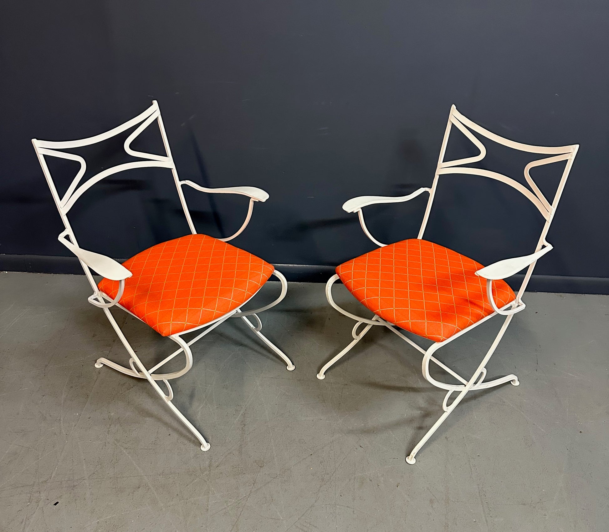 1940s French mid-century modern outdoor dining set featuring six white wrought iron chairs with orange diamond-patterned cushions and a matching table with decorative curved frames