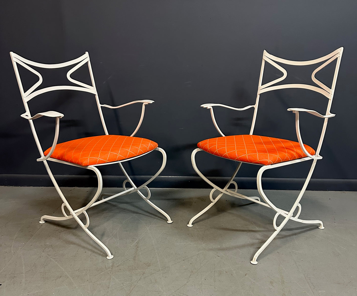 1940s French mid-century modern outdoor dining set featuring six white wrought iron chairs with orange diamond-patterned cushions and a matching table with decorative curved frames