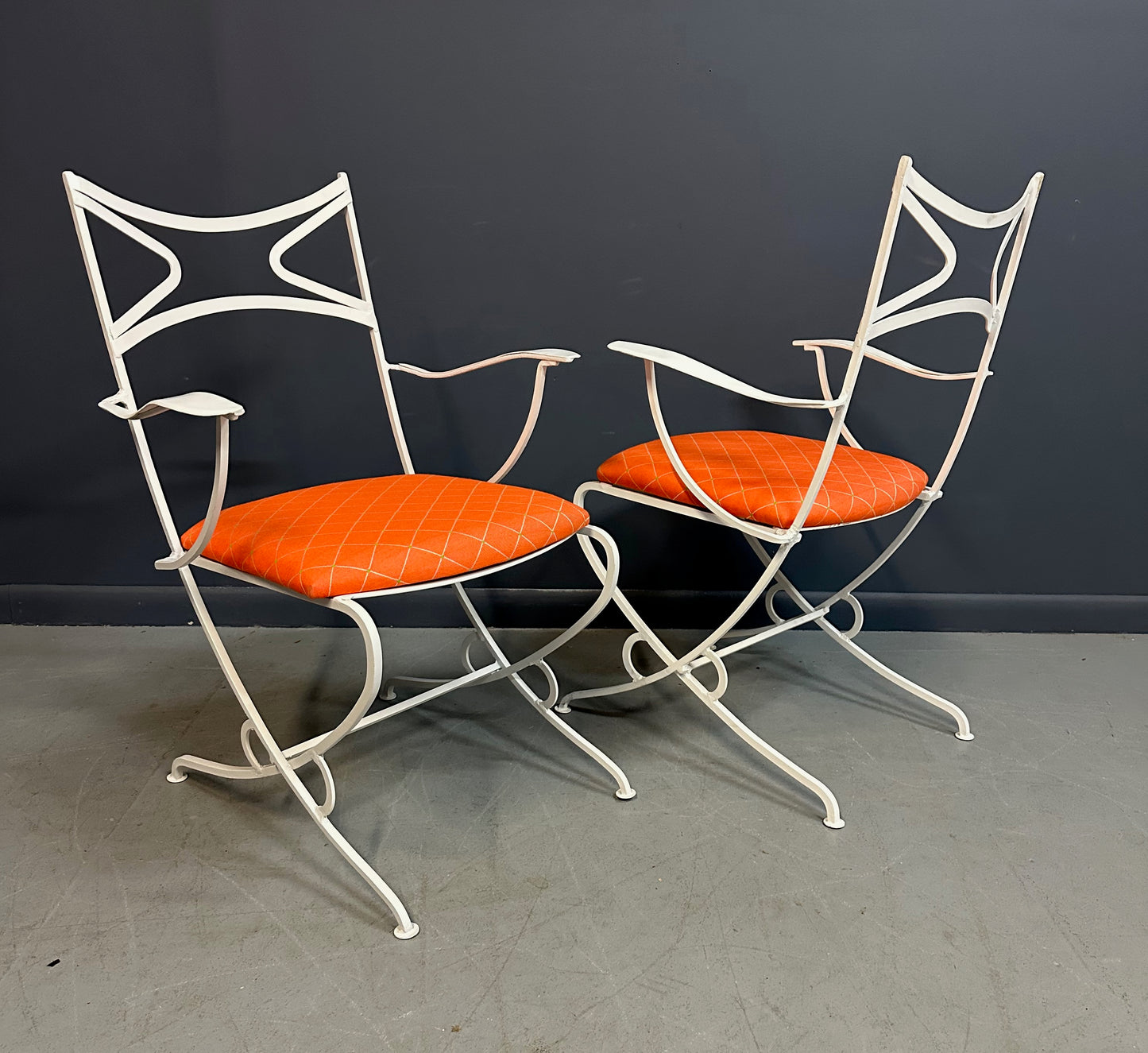 1940s French mid-century modern outdoor dining set featuring six white wrought iron chairs with orange diamond-patterned cushions and a matching table with decorative curved frames