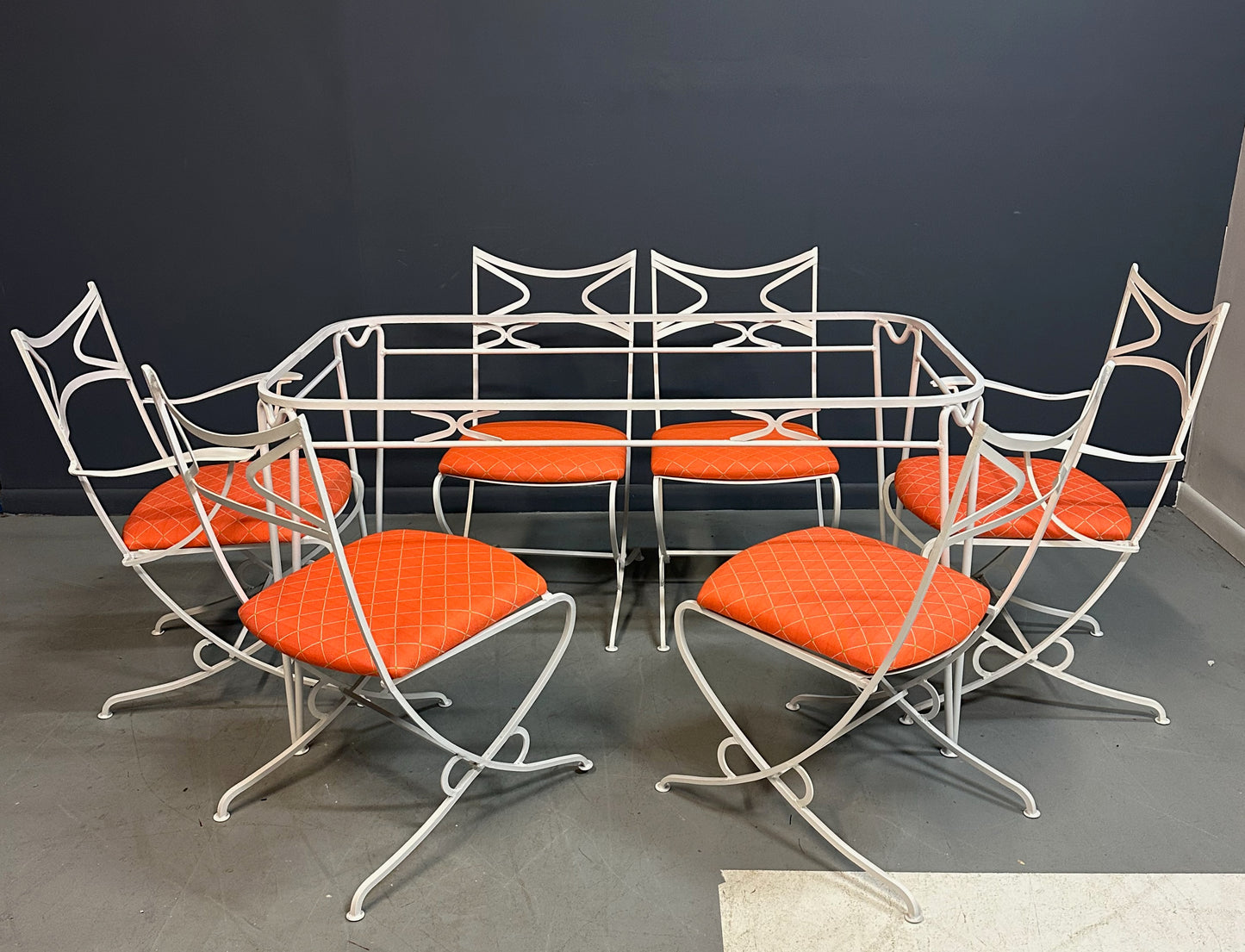1940s French mid-century modern outdoor dining set featuring six white wrought iron chairs with orange diamond-patterned cushions and a matching table with decorative curved frames