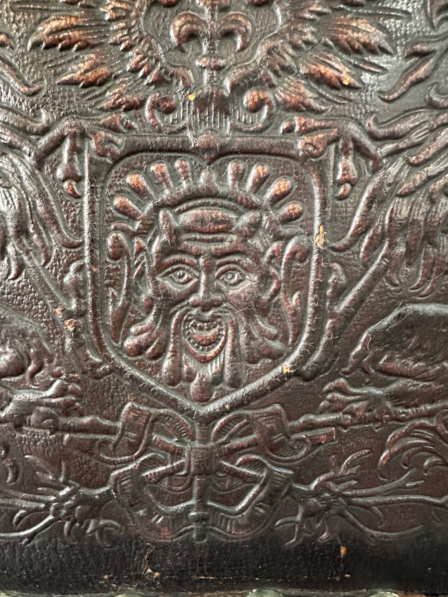 Impressive English 18th-century oak carved armchair featuring tooled leather backrest with heraldic motif, nailhead trim, and ornate turned wood detailing