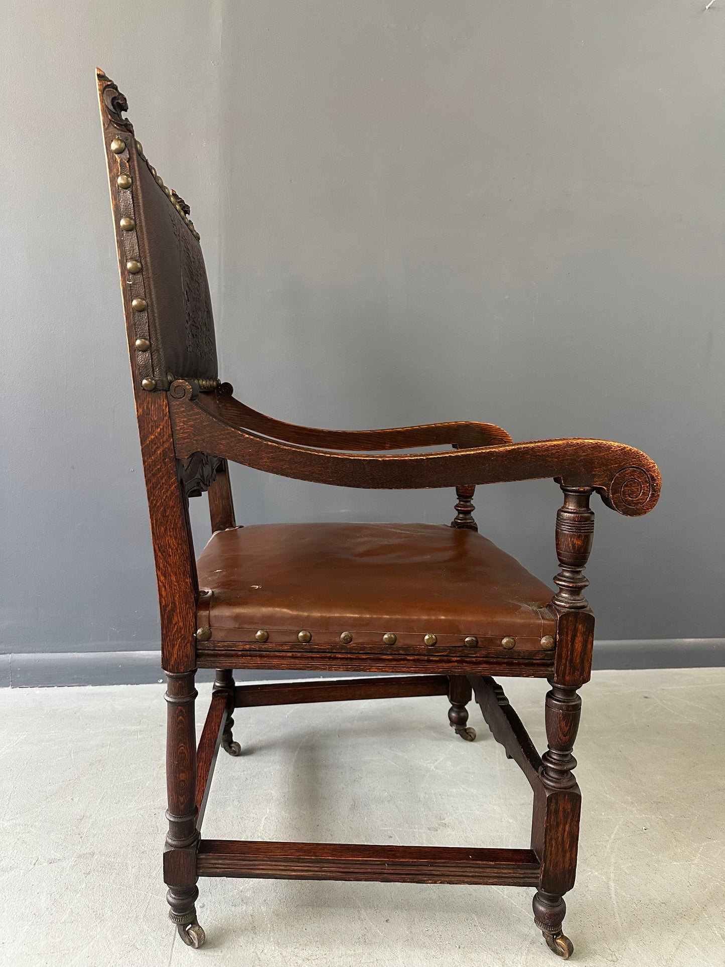 Impressive English 18th-century oak carved armchair featuring tooled leather backrest with heraldic motif, nailhead trim, and ornate turned wood detailing